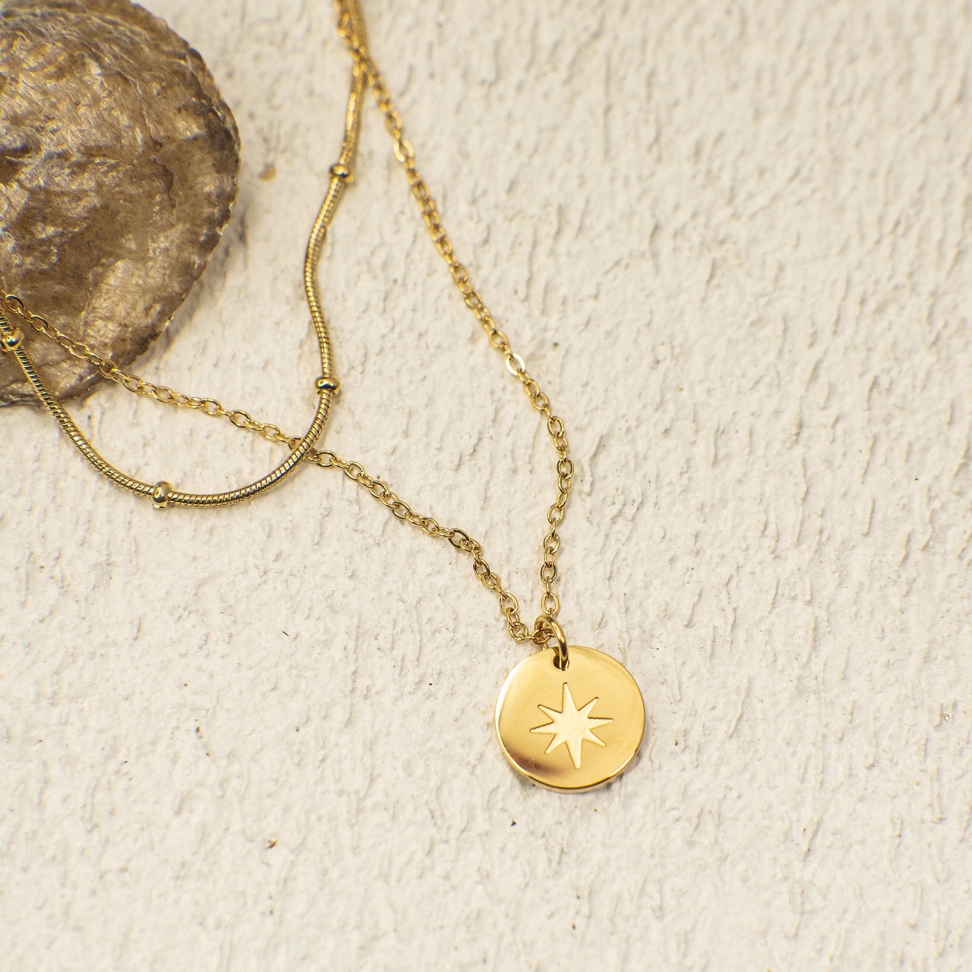 Gold necklace with a star pendant on a textured beige surface
