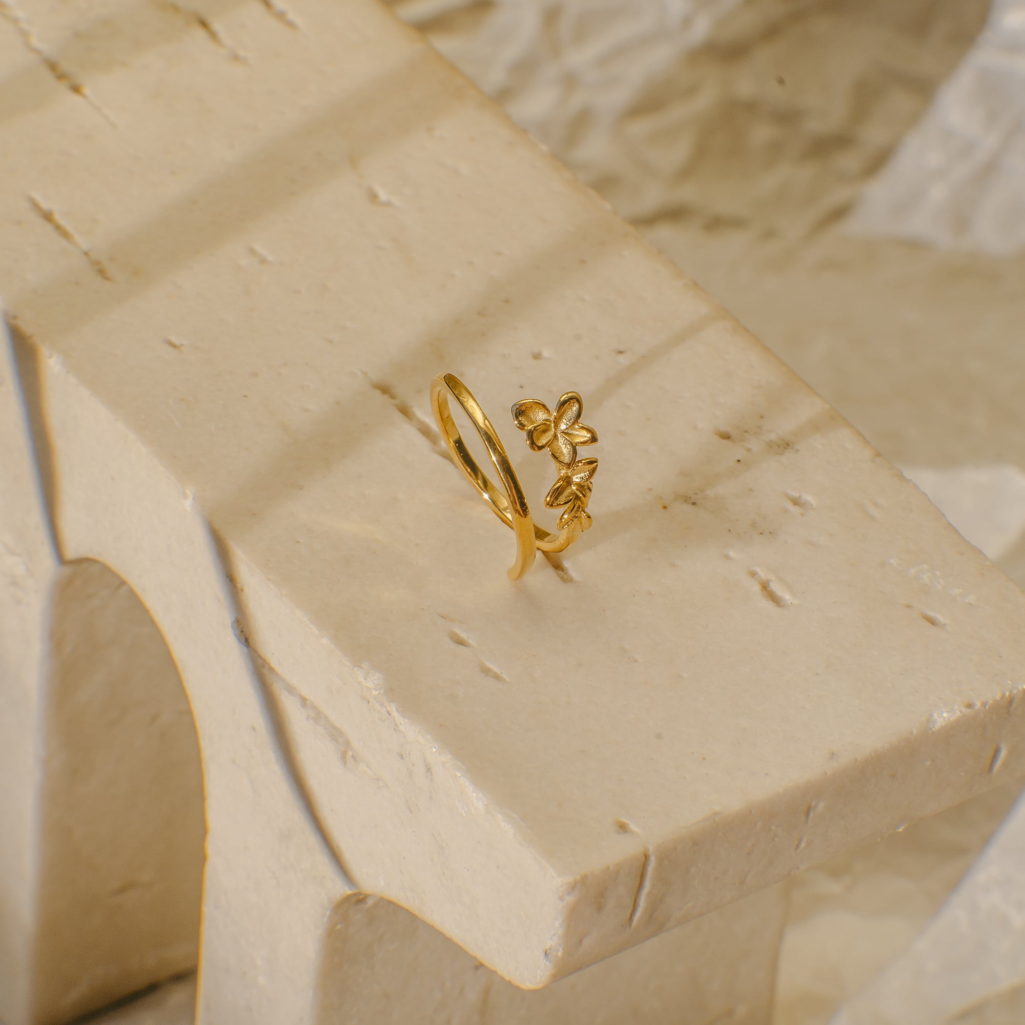 Gold ring with a floral design on a beige stone surface
