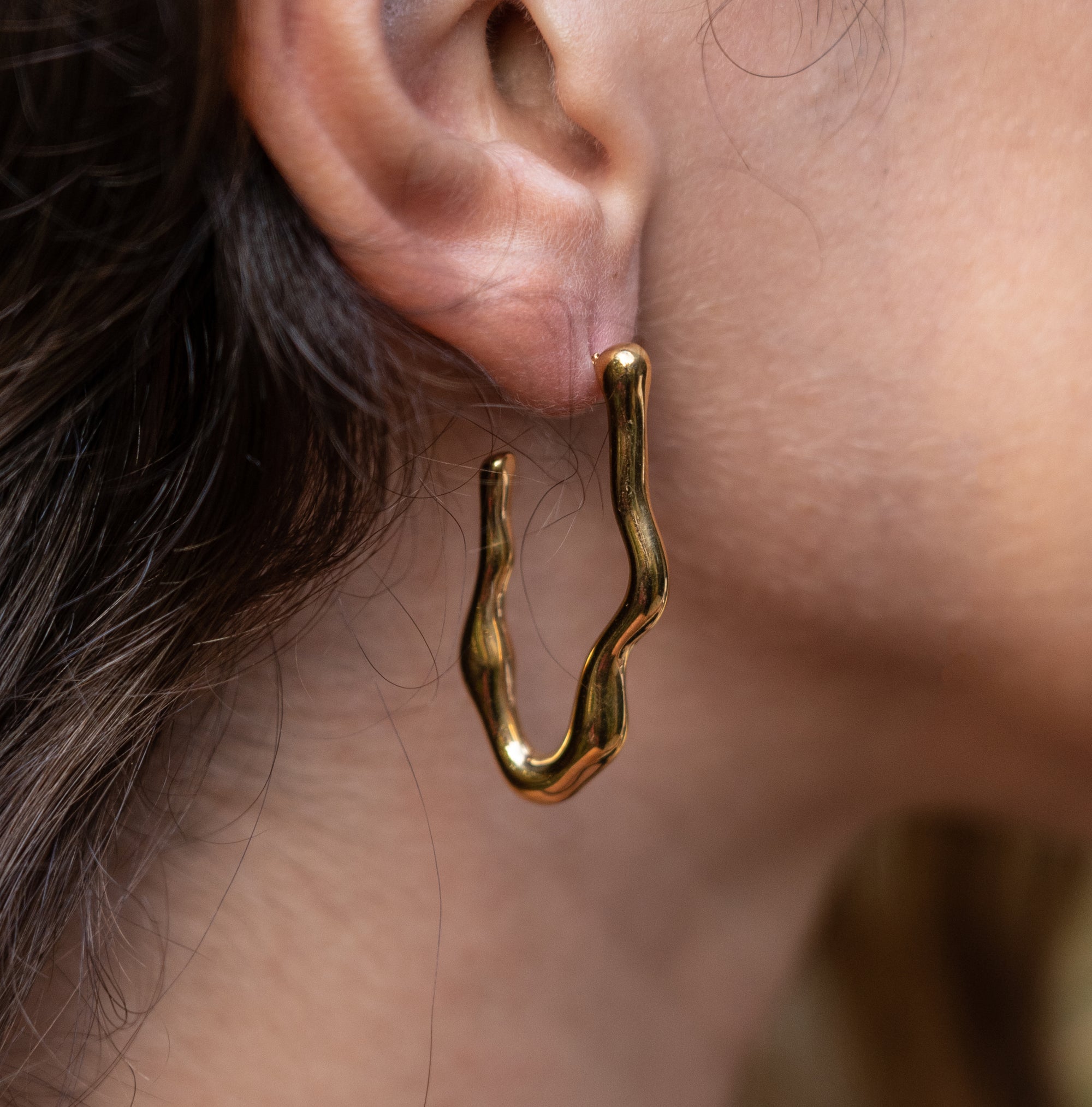A model wearing a curvy gold earring