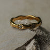 Gold ring with floral designs and small stones on a textured surface