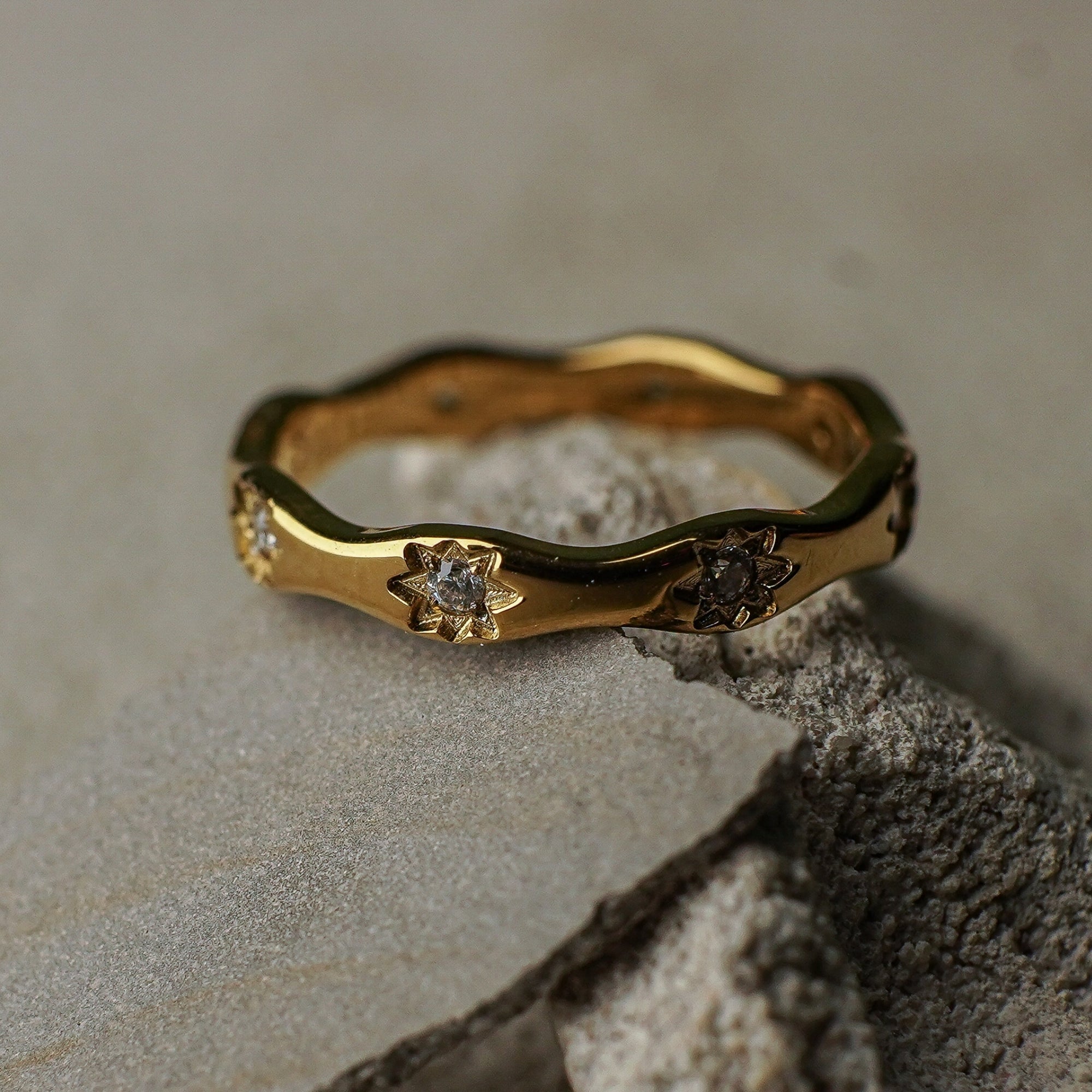 Gold ring with floral designs and small stones on a textured surface