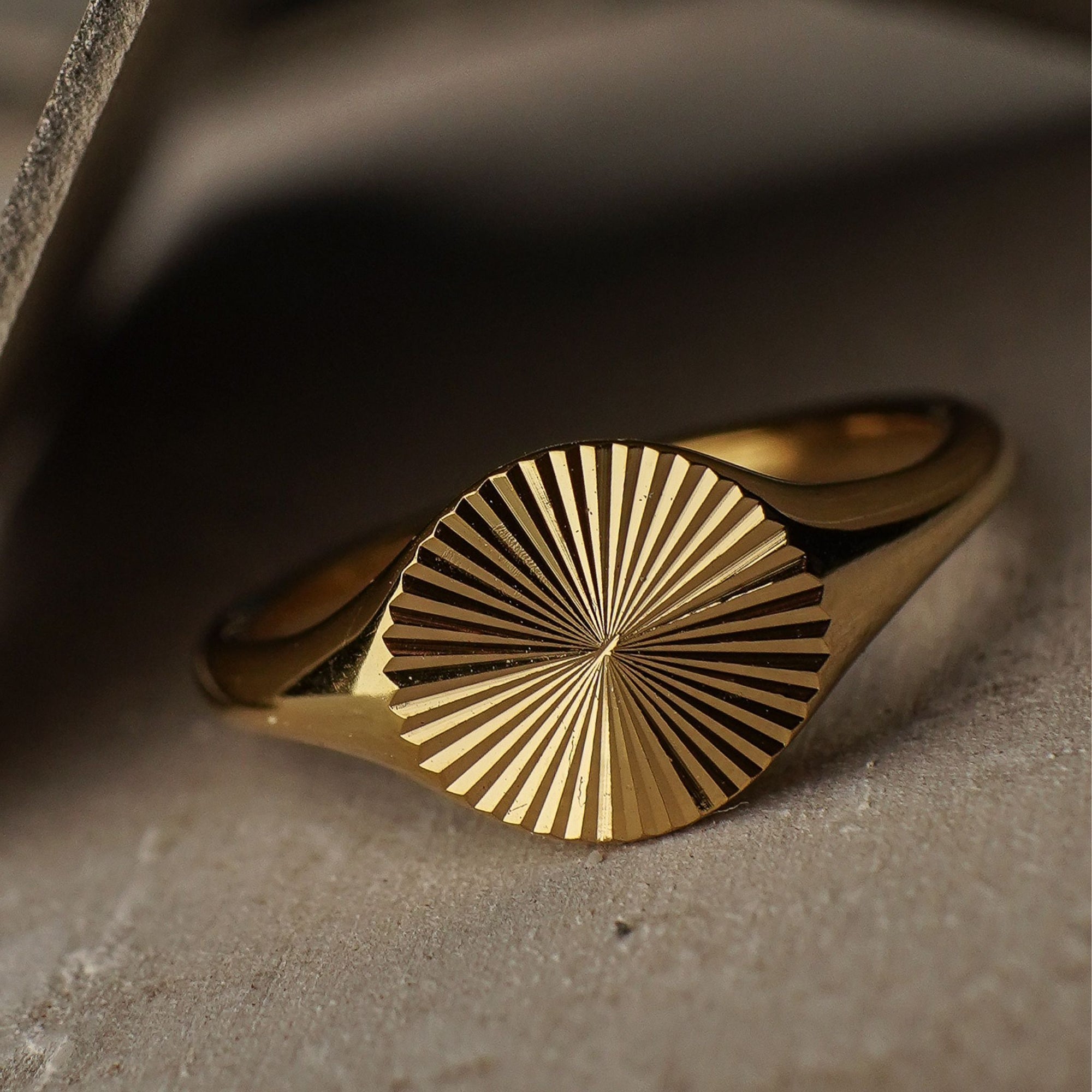 Gold ring with sunburst design on a textured surface