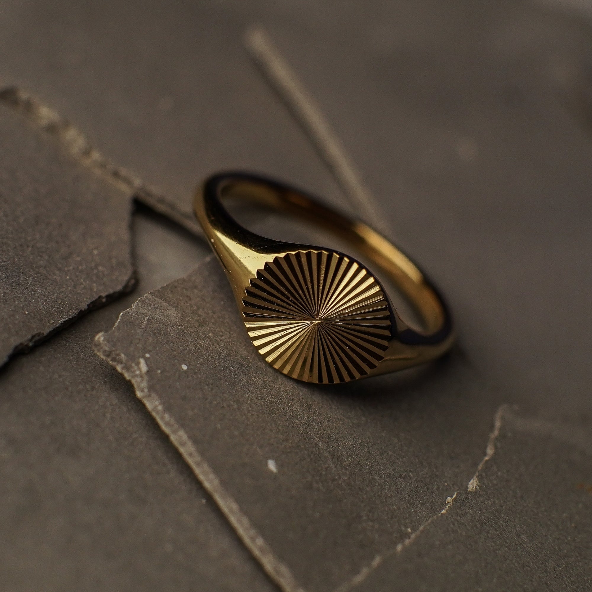 Gold ring with sunburst design on a dark stone surface