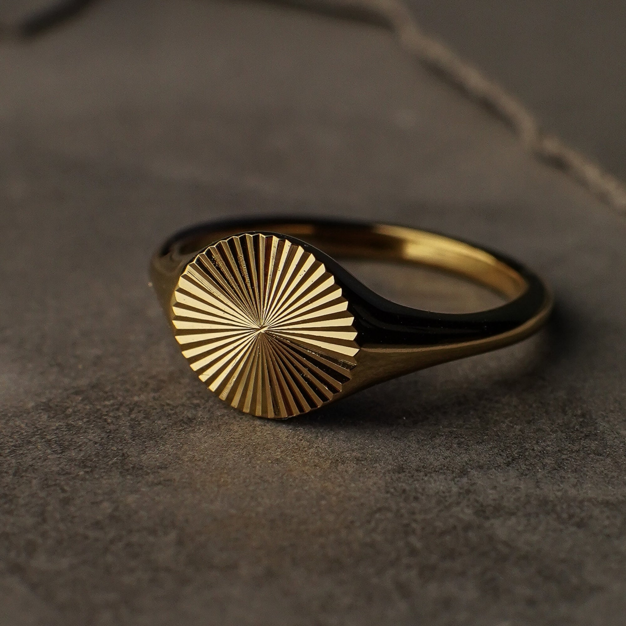 Gold ring with sunburst design on a dark surface