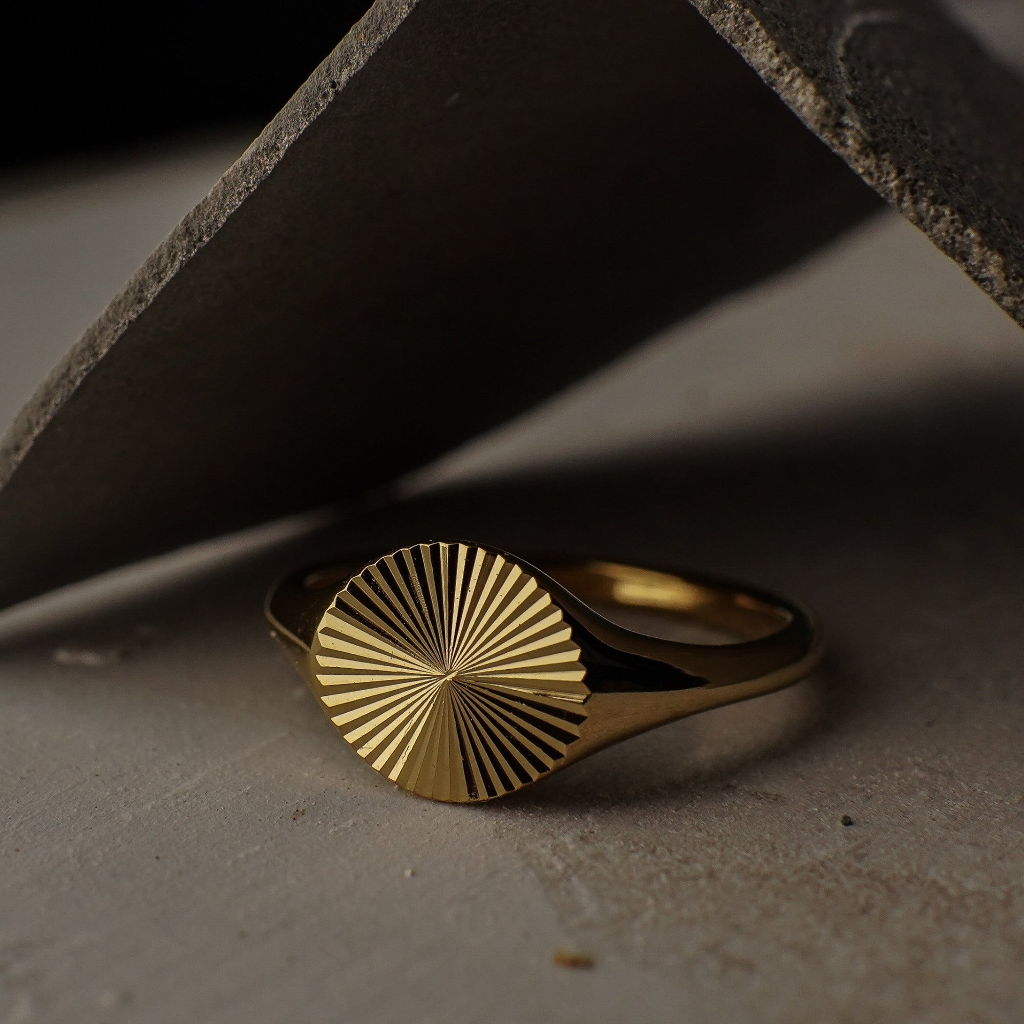 Gold ring with sunburst design on a textured surface