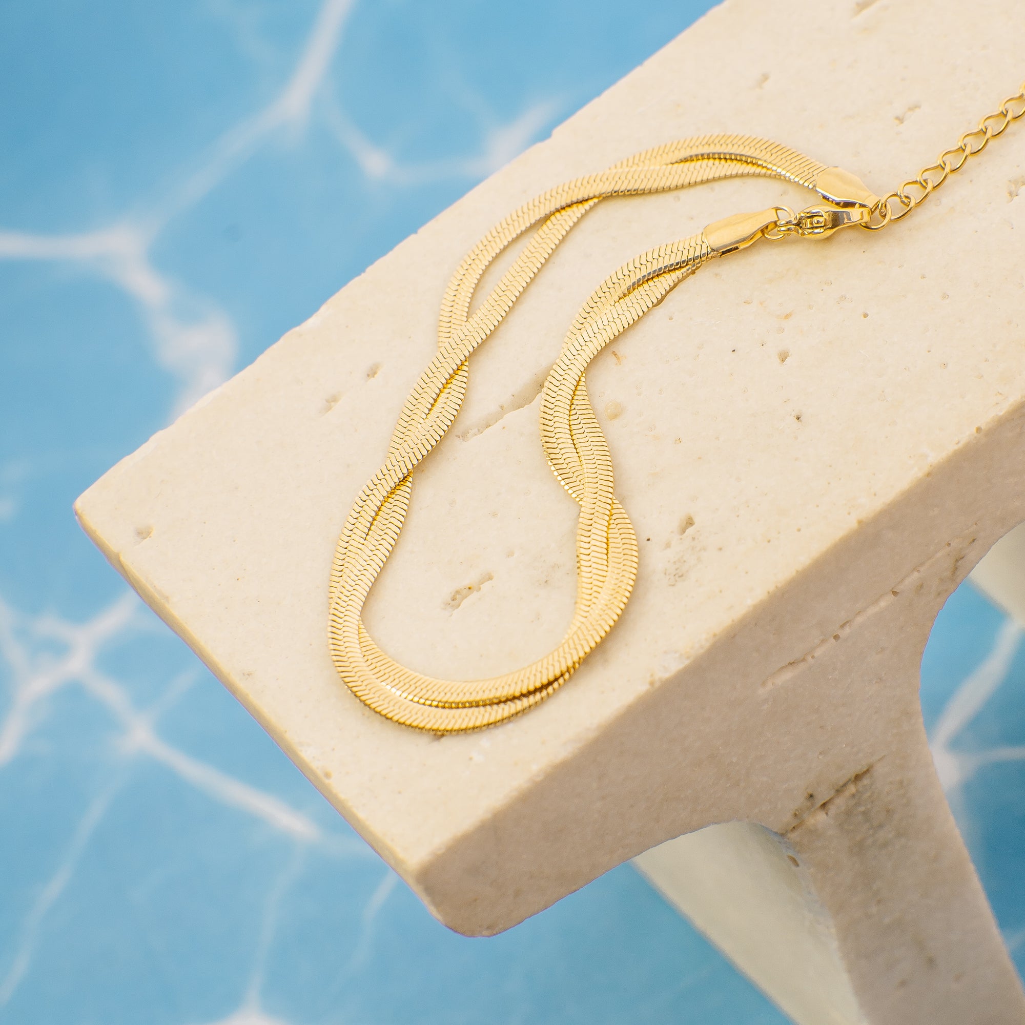 Gold necklace on a beige stand with a blue water background