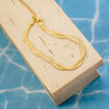 Gold necklace on a beige display block with a blue textured background