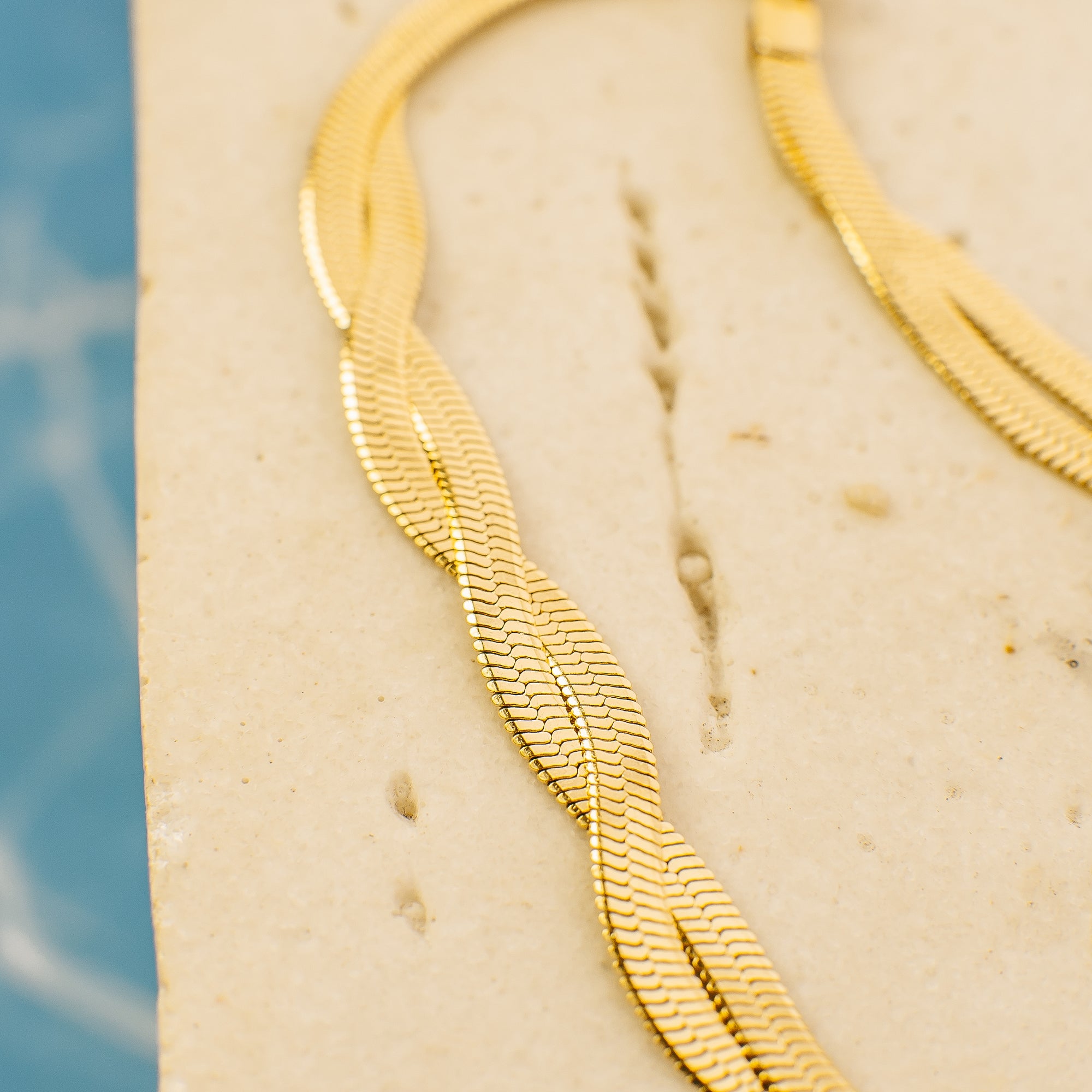 Close-up of a gold necklace on a textured beige surface with a blurred blue background