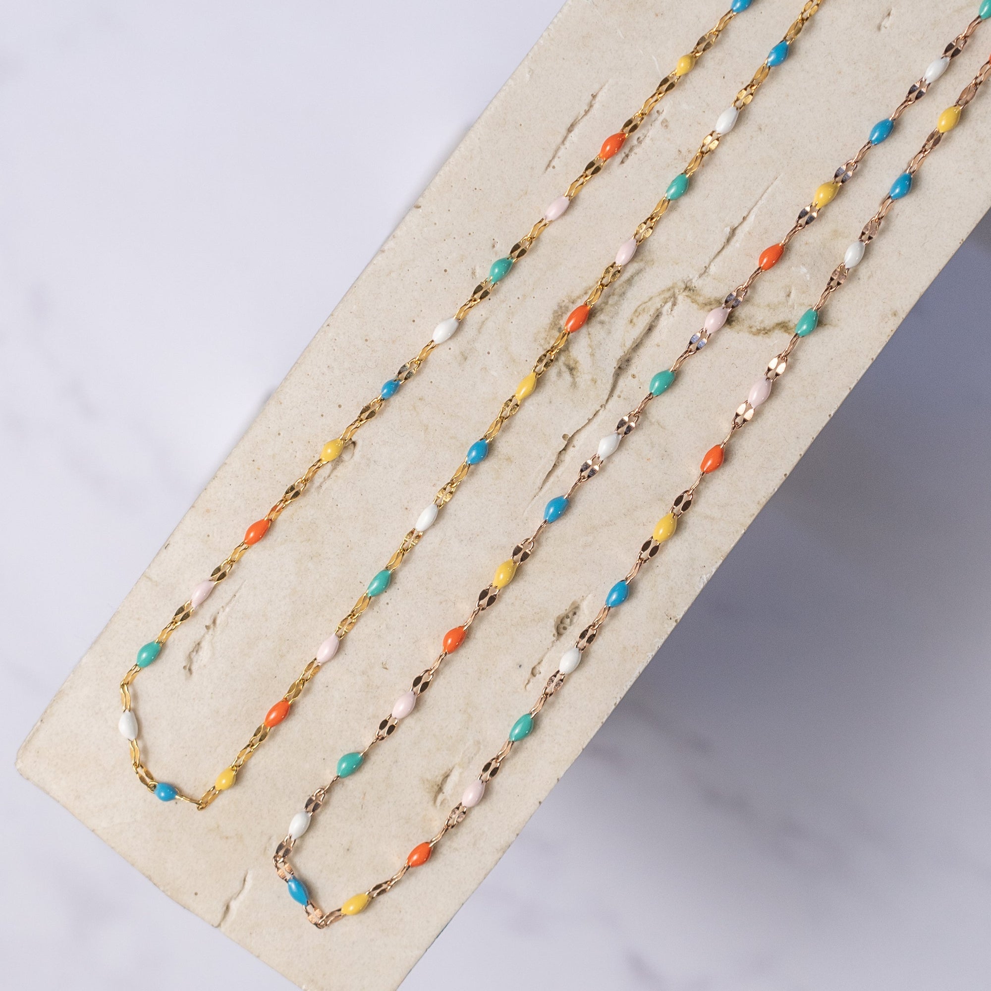 Two colorful beaded choker necklaces displayed on a wooden surface, with a combination of metallic and matte beads in a rainbow pattern.