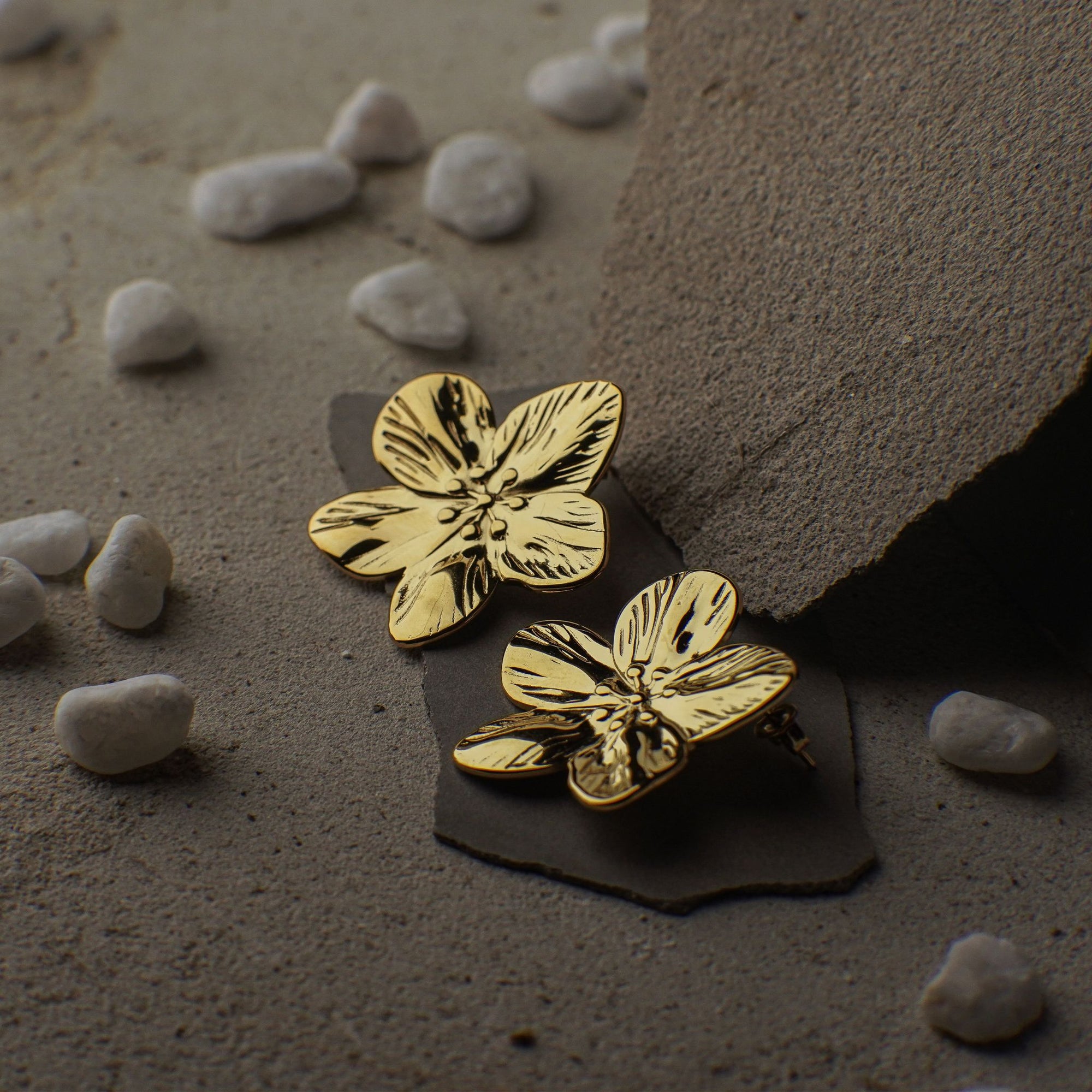 Gold floral earrings on a textured surface with small stones around