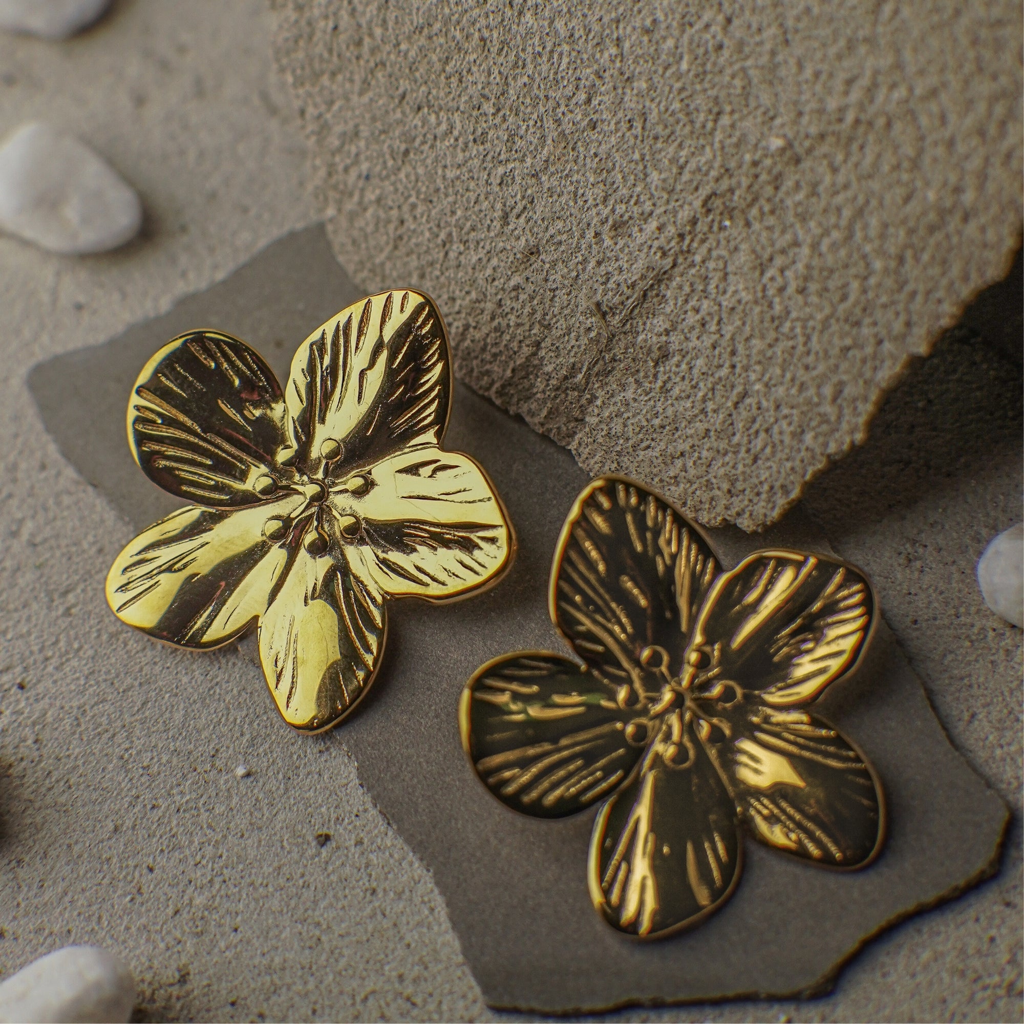 Gold floral earrings on a textured stone surface