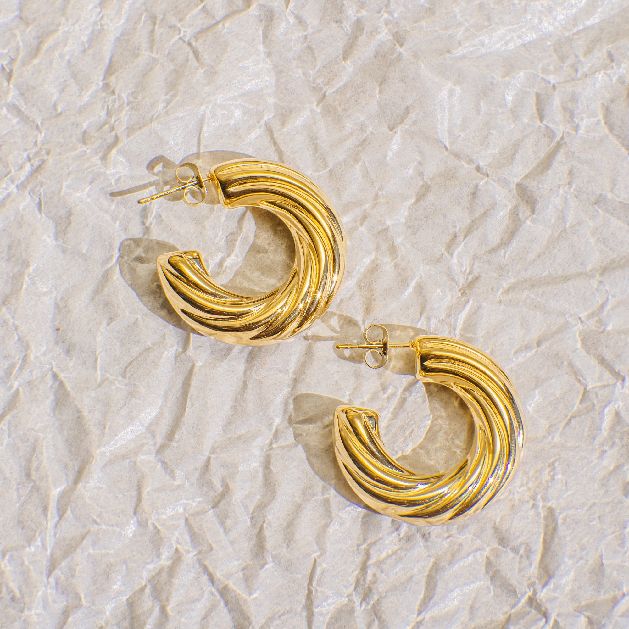 Gold hoop earrings on a textured beige background