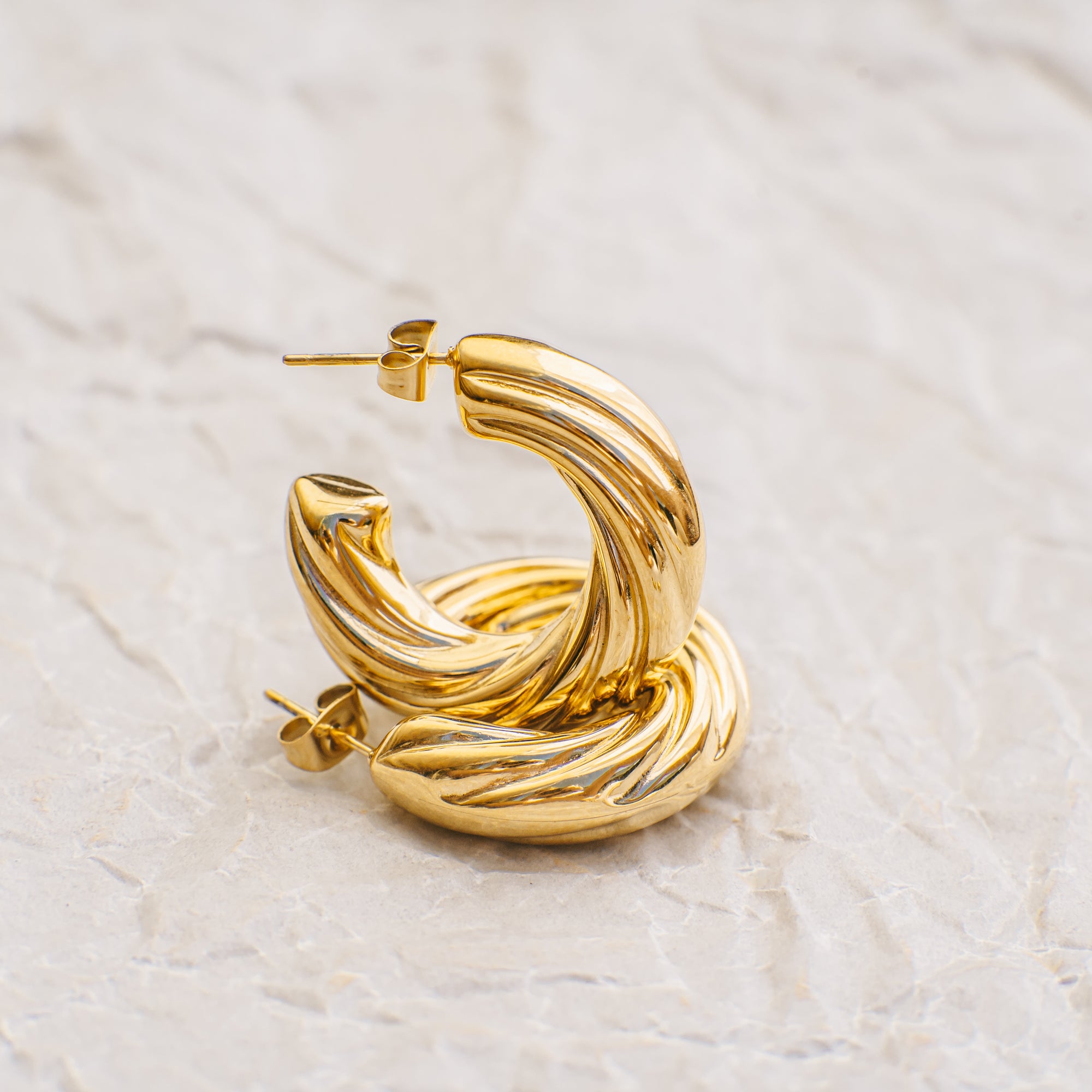 Gold hoop earrings on a light beige marble surface