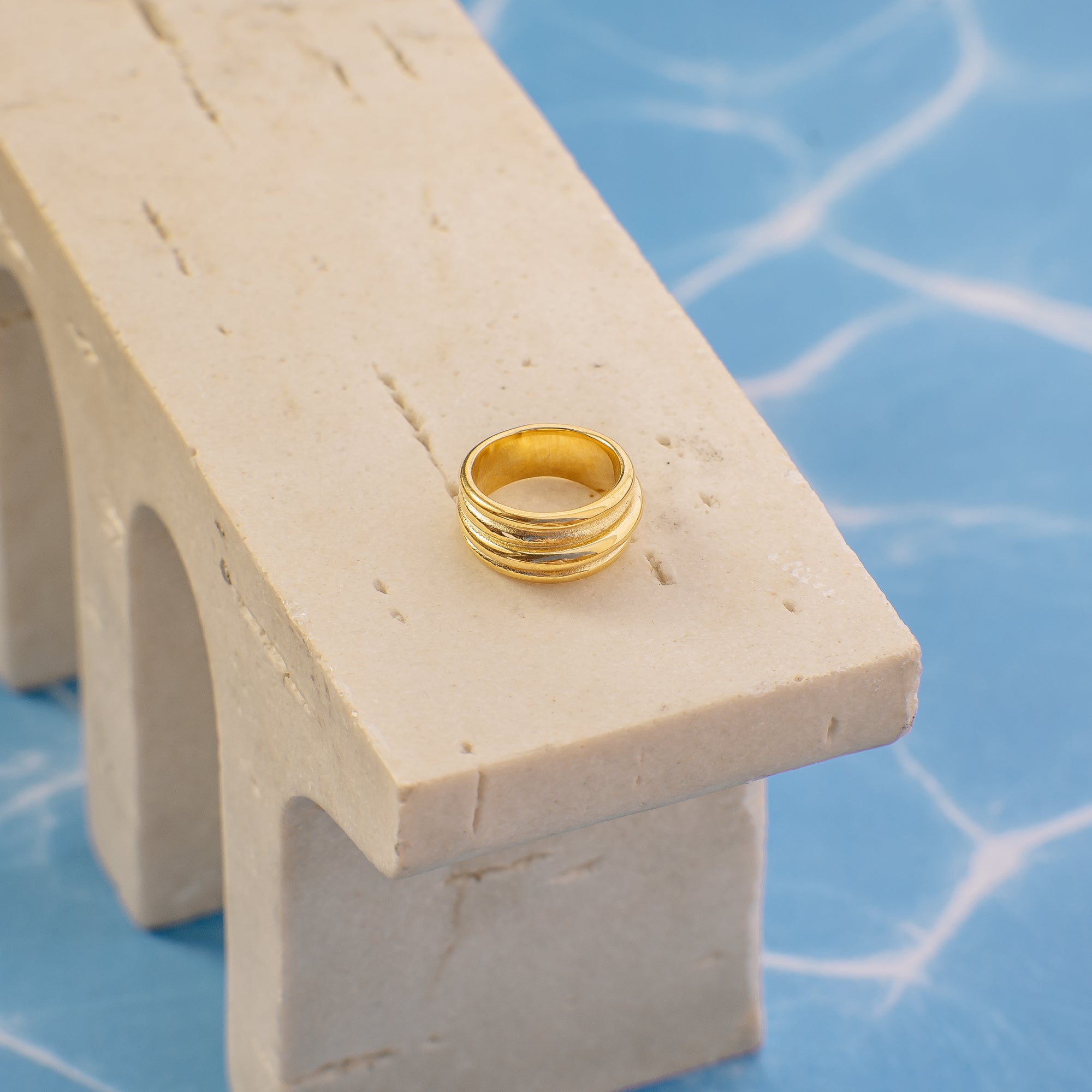 Gold ring on a small stone archway with a blue water background