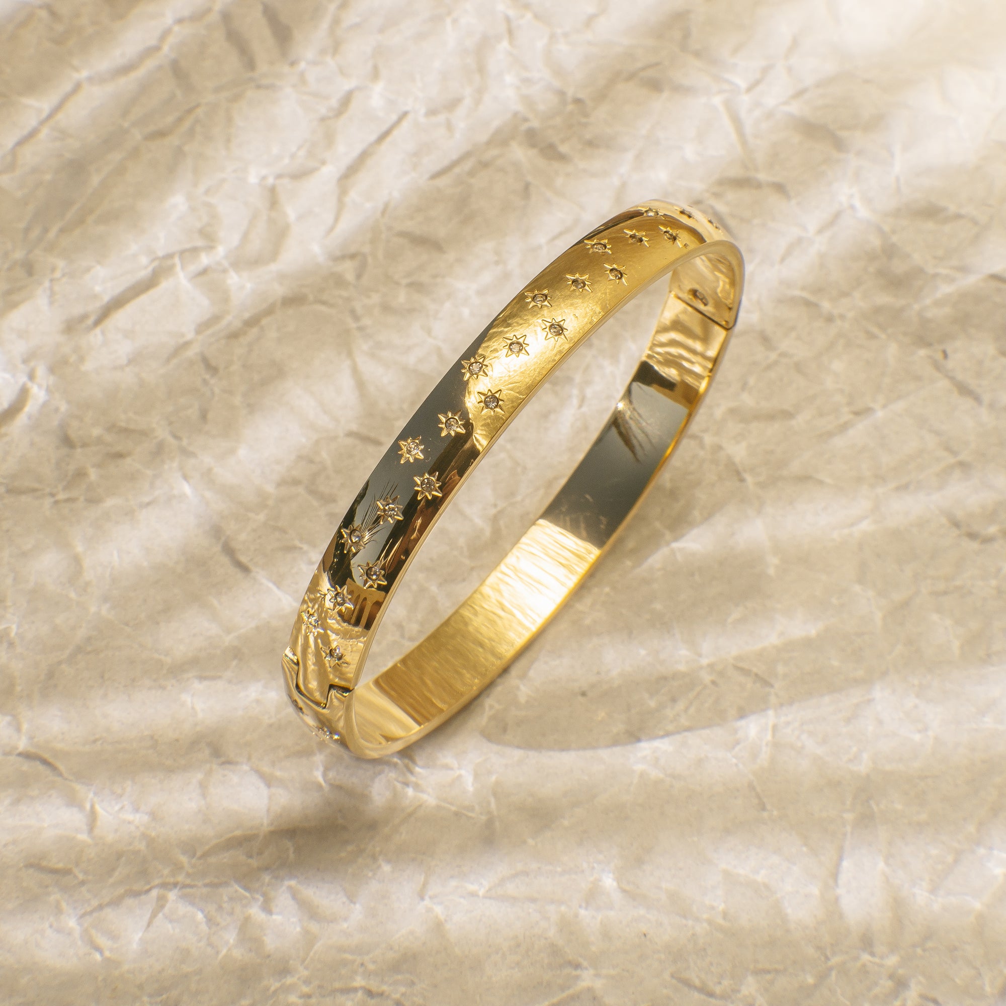 Gold bracelet with star patterns on a textured beige background