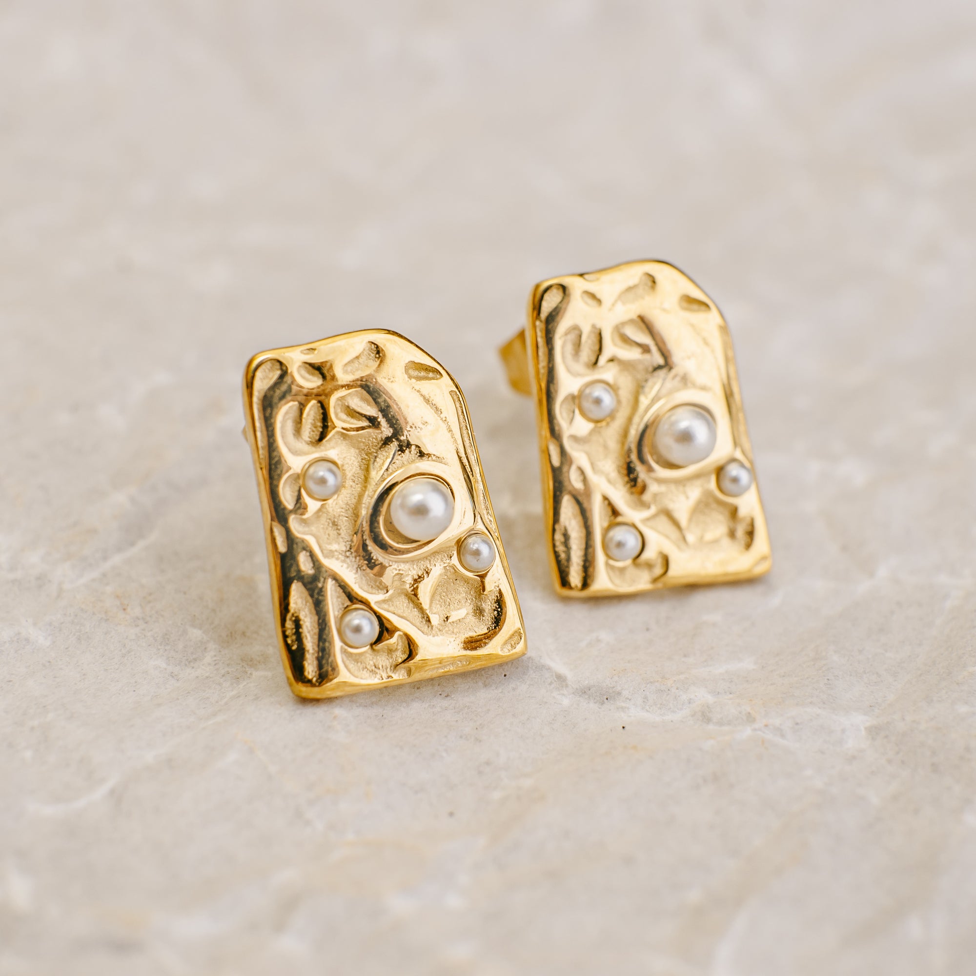 Gold earrings with pearl accents on a beige marble background