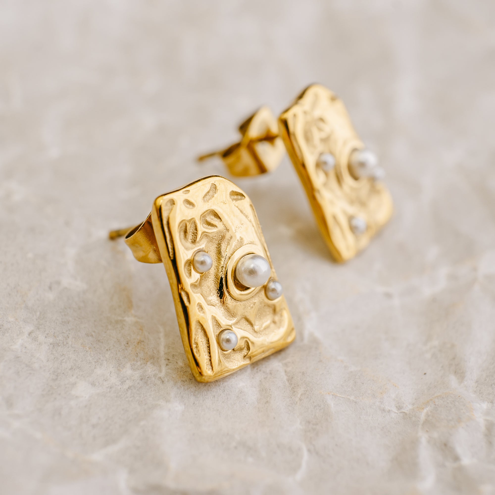 Gold earrings with pearl accents on a beige background