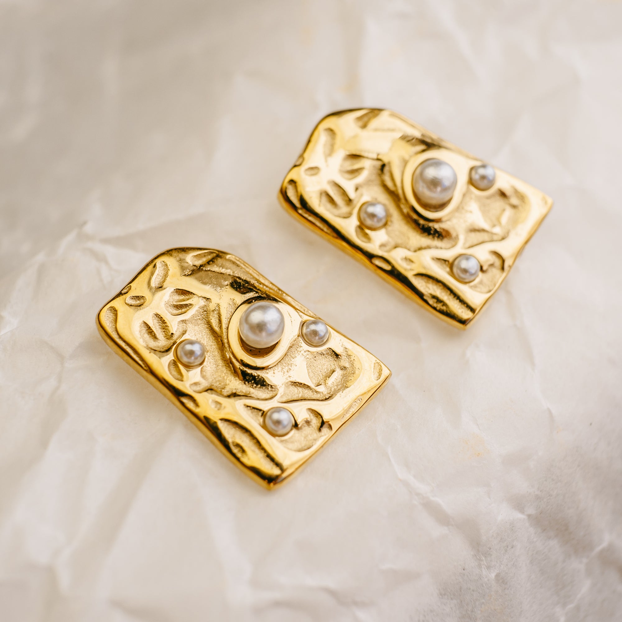 Pair of gold earrings with pearl-like stones on a beige fabric background