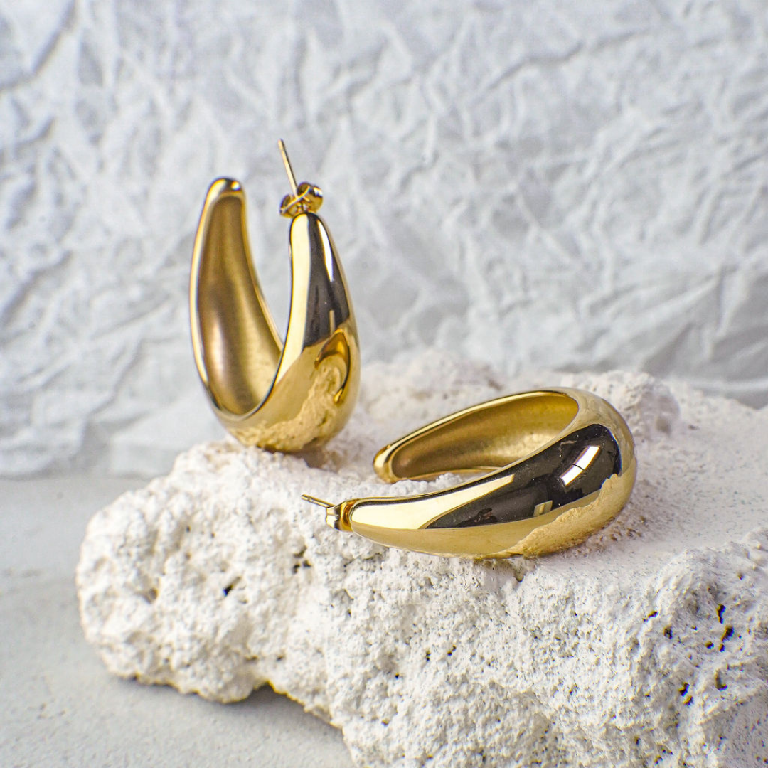 Gold hoop earrings on a textured white surface with a light gray background