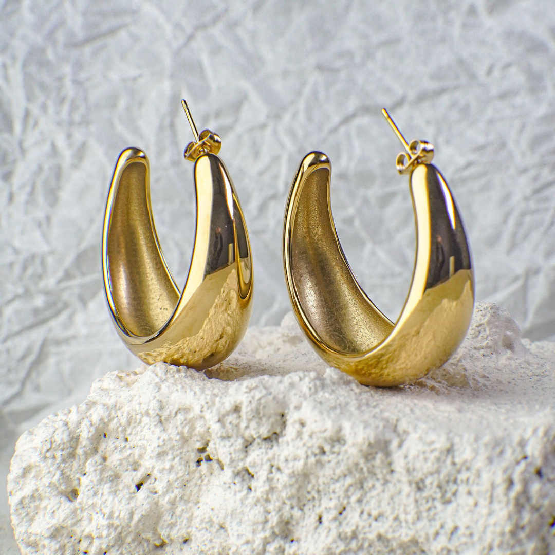 Gold hoop earrings on a textured white surface with a light gray background
