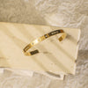 Gold bracelet with embedded stones on a beige stone surface