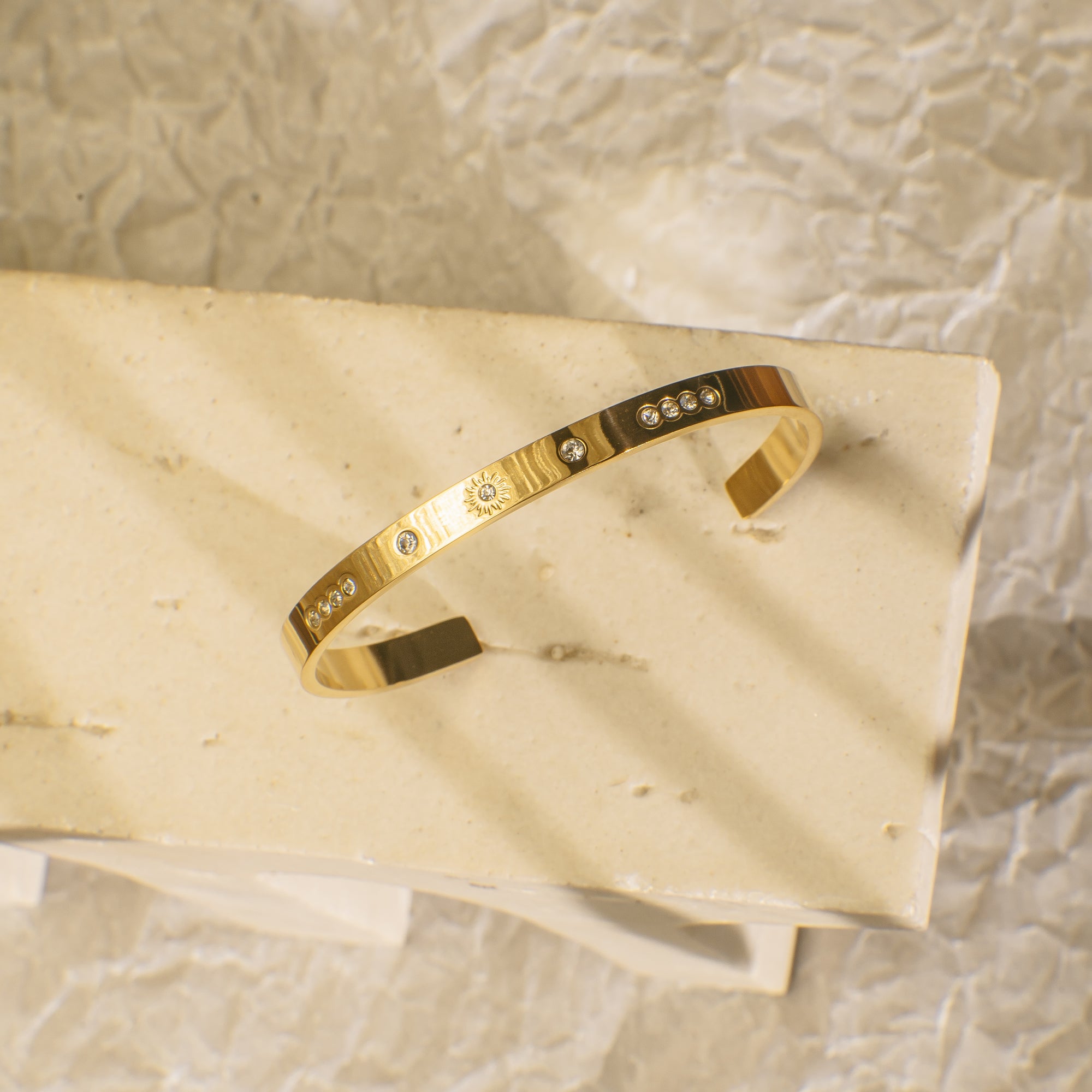 Gold bracelet with embedded stones on a beige stone surface