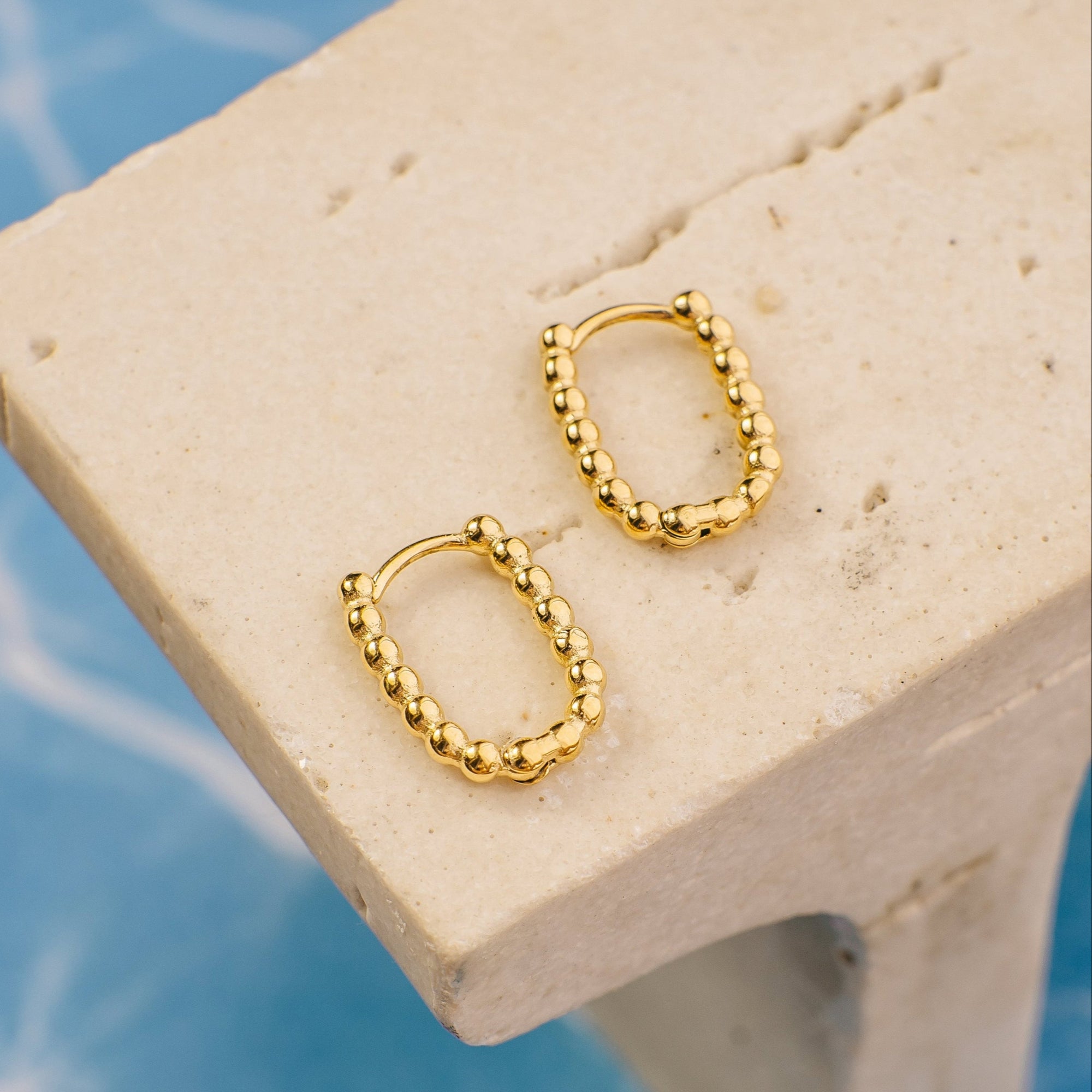 Gold hoop earrings on a beige stone surface with a blue marble background