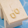 Gold hoop earrings on a beige stand with a blue geometric background