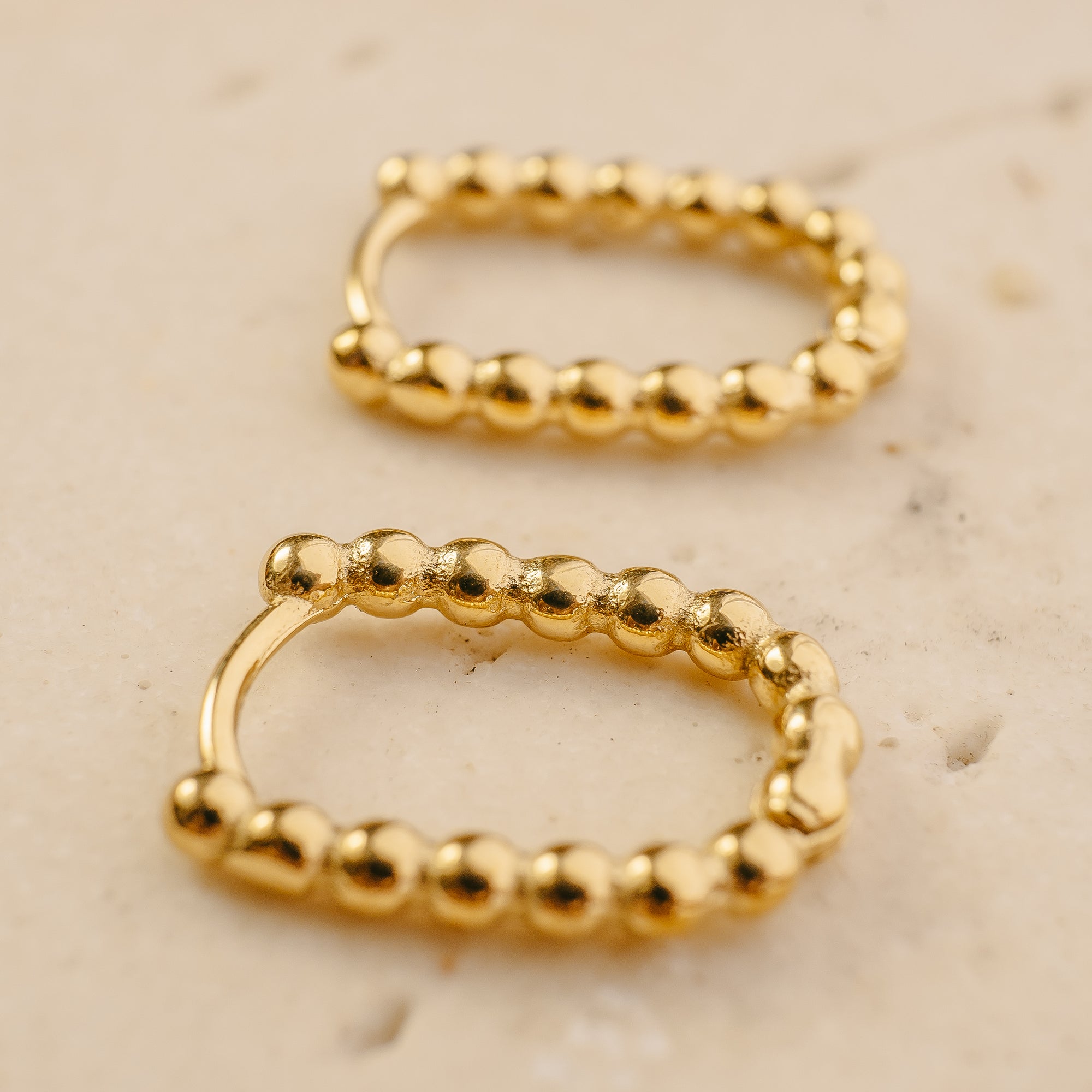 Two gold hoop earrings on a beige surface
