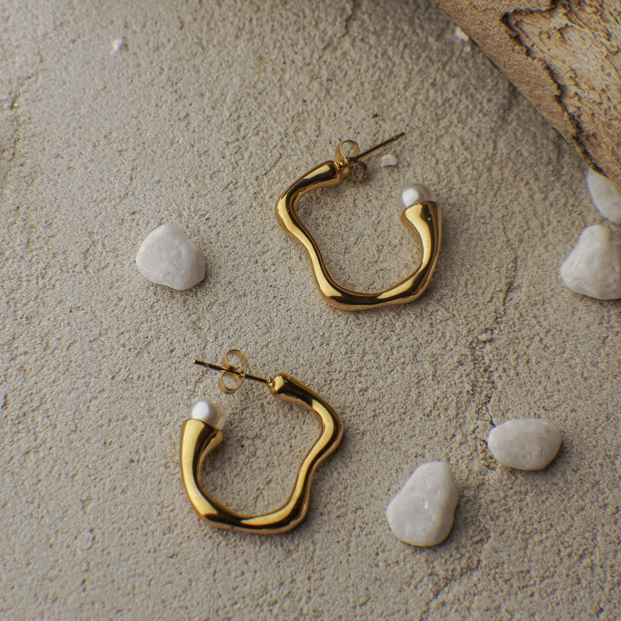 Gold hoop earrings on a sandy surface with small stones