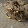 Gold hoop earrings with pearls on a sandy surface