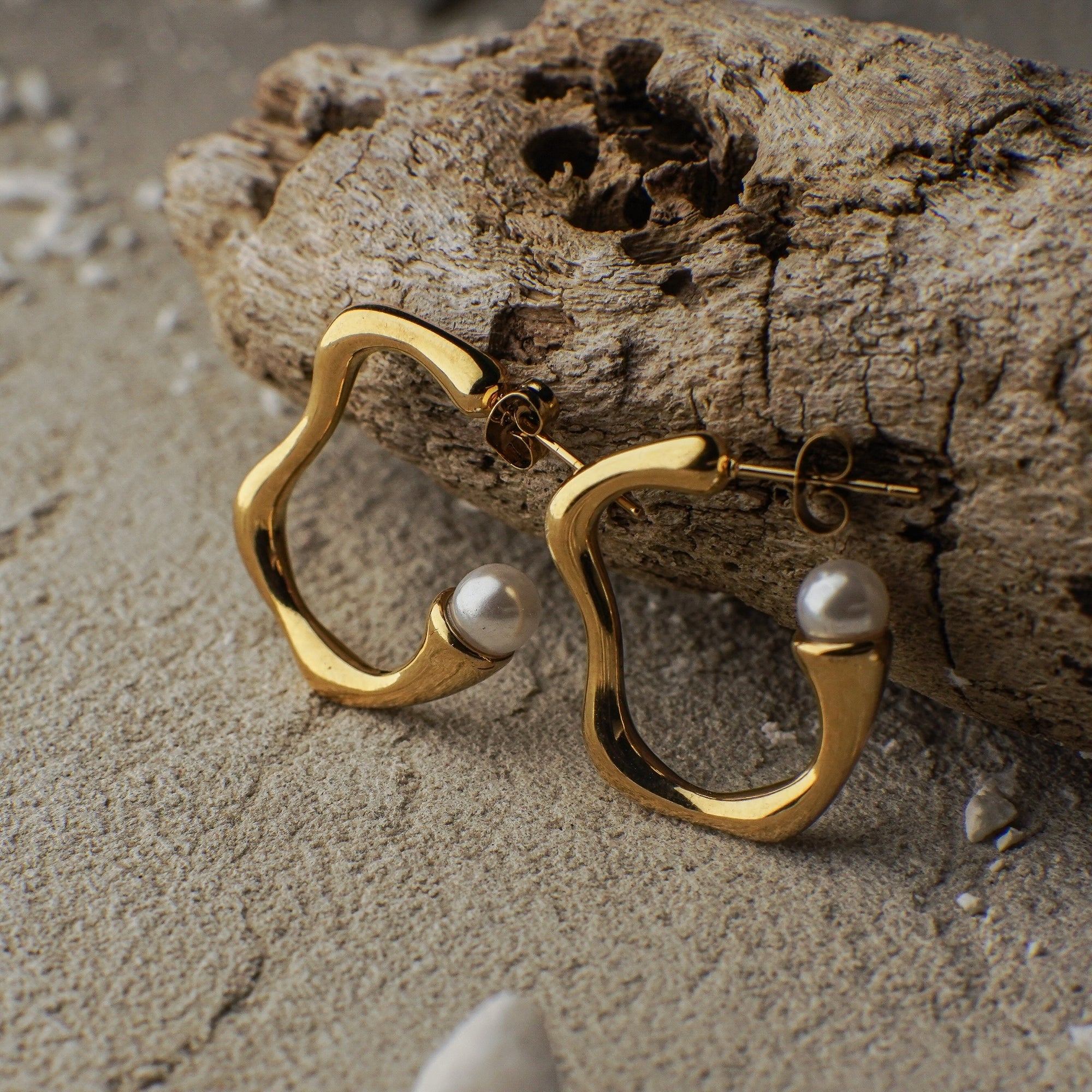 Gold hoop earrings with pearls on a sandy surface