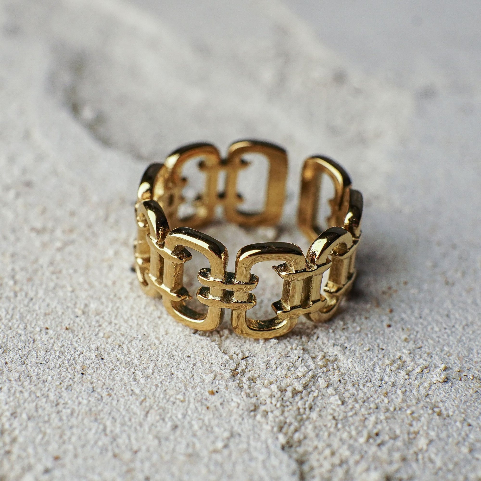 Gold chain-link ring on a sandy surface