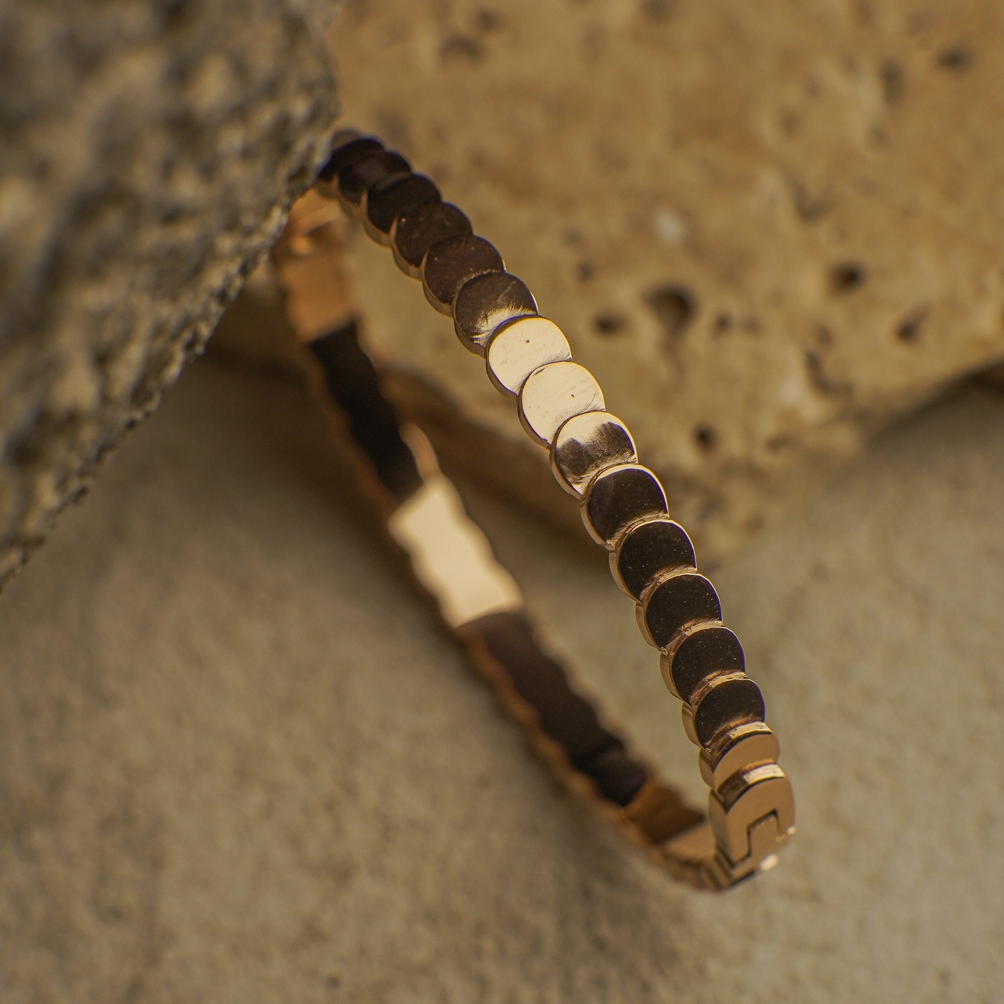 Gold bracelet with black beads on a textured stone surface