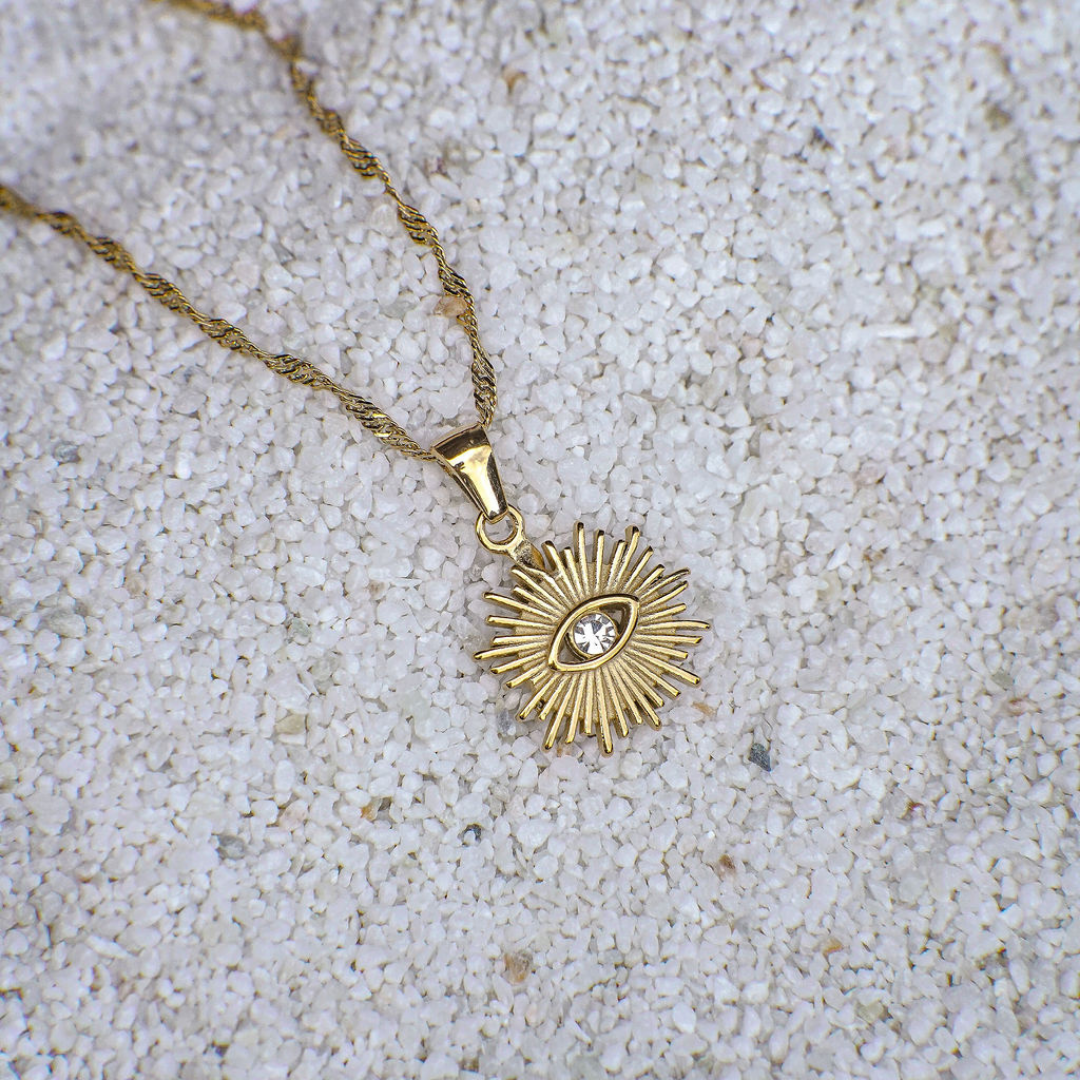 Gold necklace with a sun-shaped pendant on a sandy background