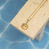 Gold necklace with a sun-shaped pendant on a beige stand against a blue background