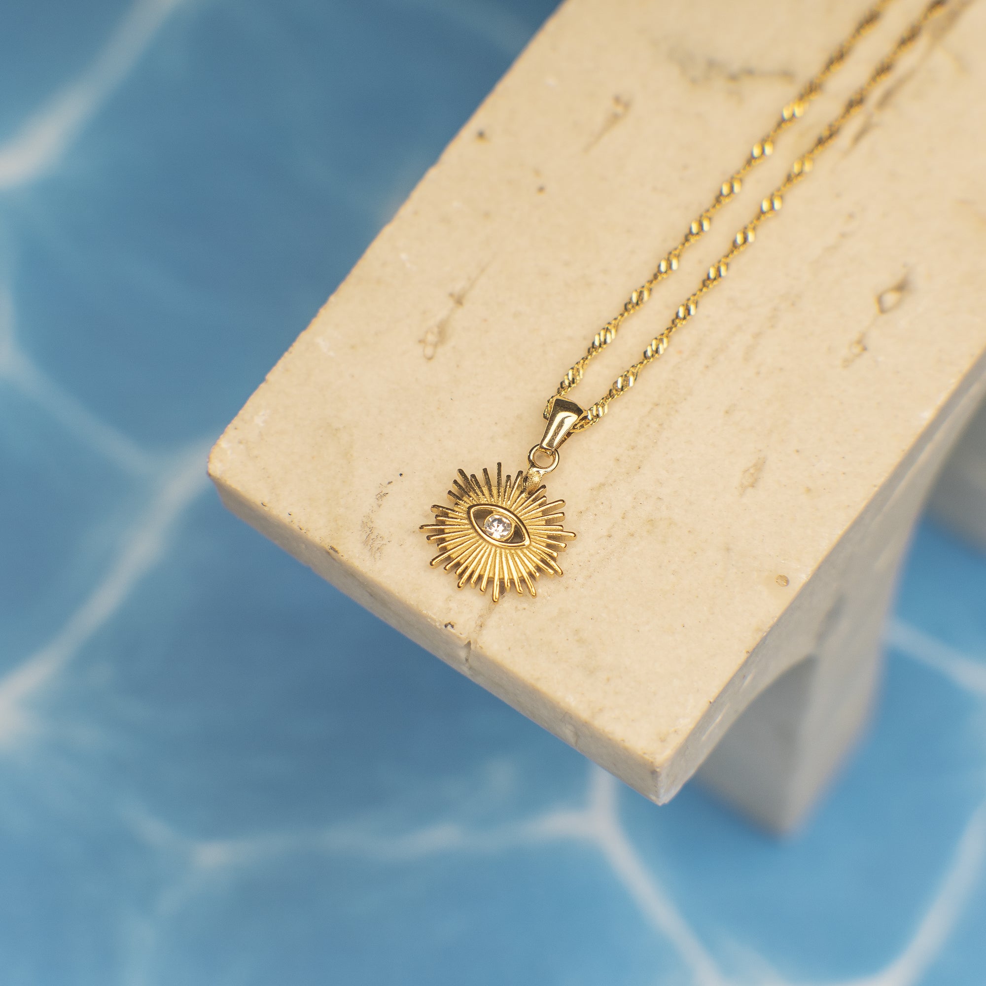 Gold necklace with a sun-shaped pendant on a beige stand against a blue background
