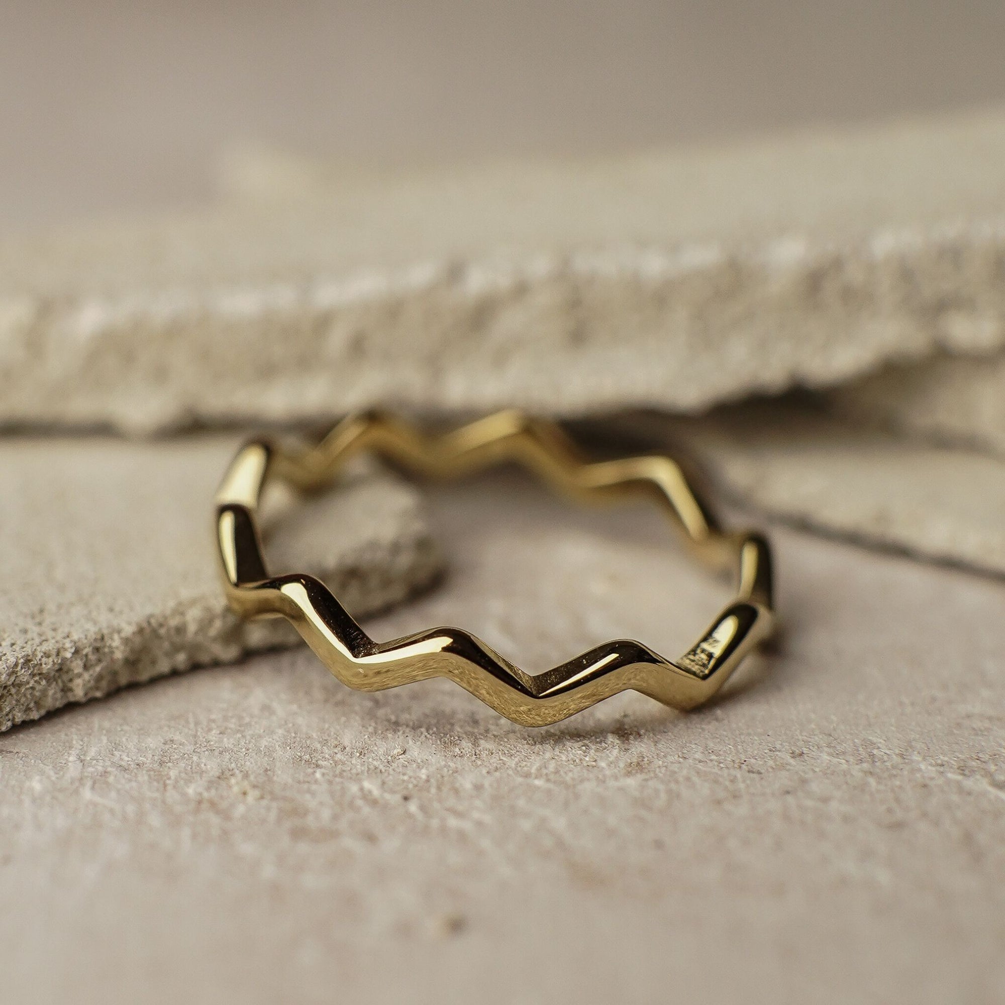 Gold ring with zigzag design on a textured surface