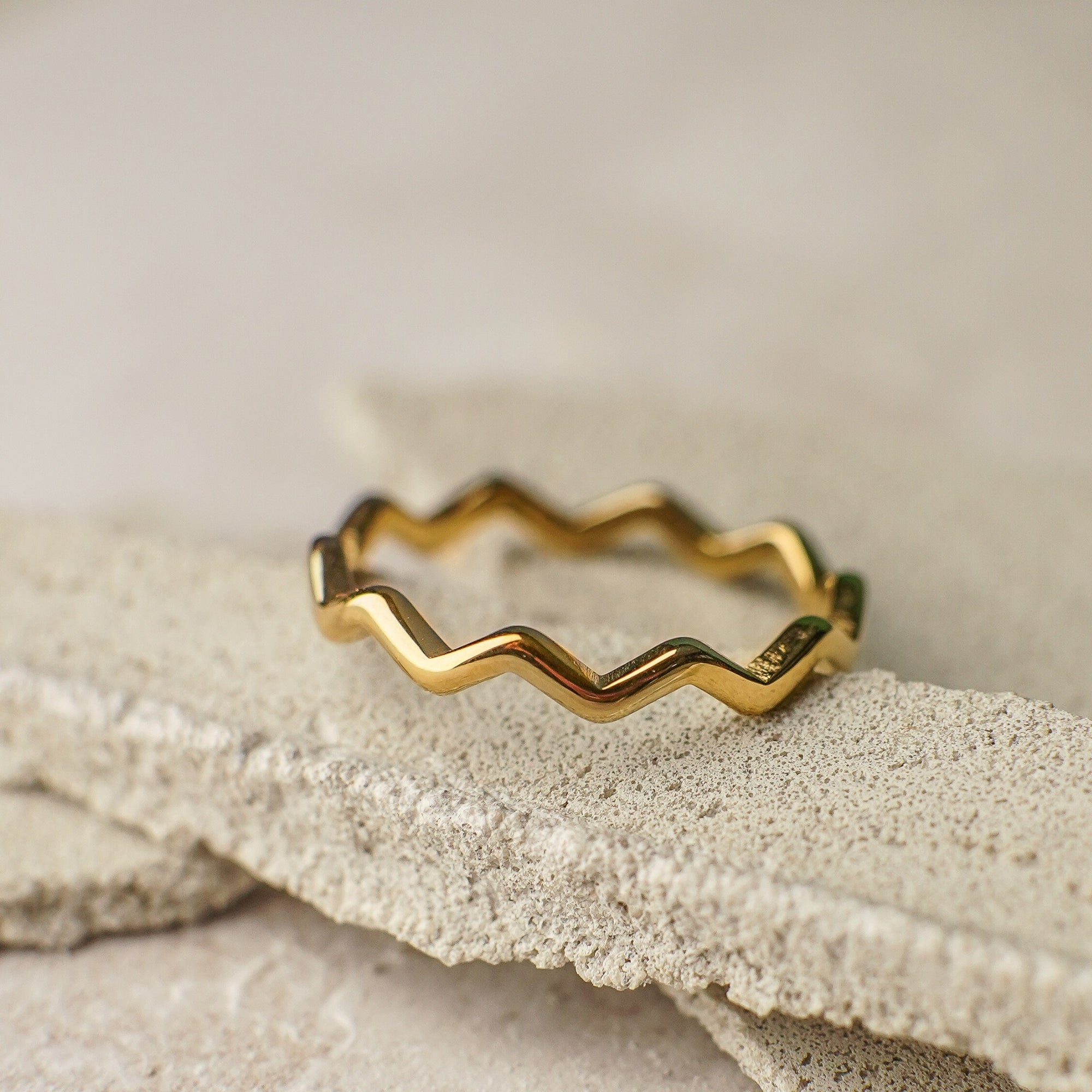 Gold ring with a zigzag design on a textured stone surface