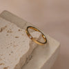 A gold-colored band ring with a zirconia centerpiece resting on a textured stone surface.