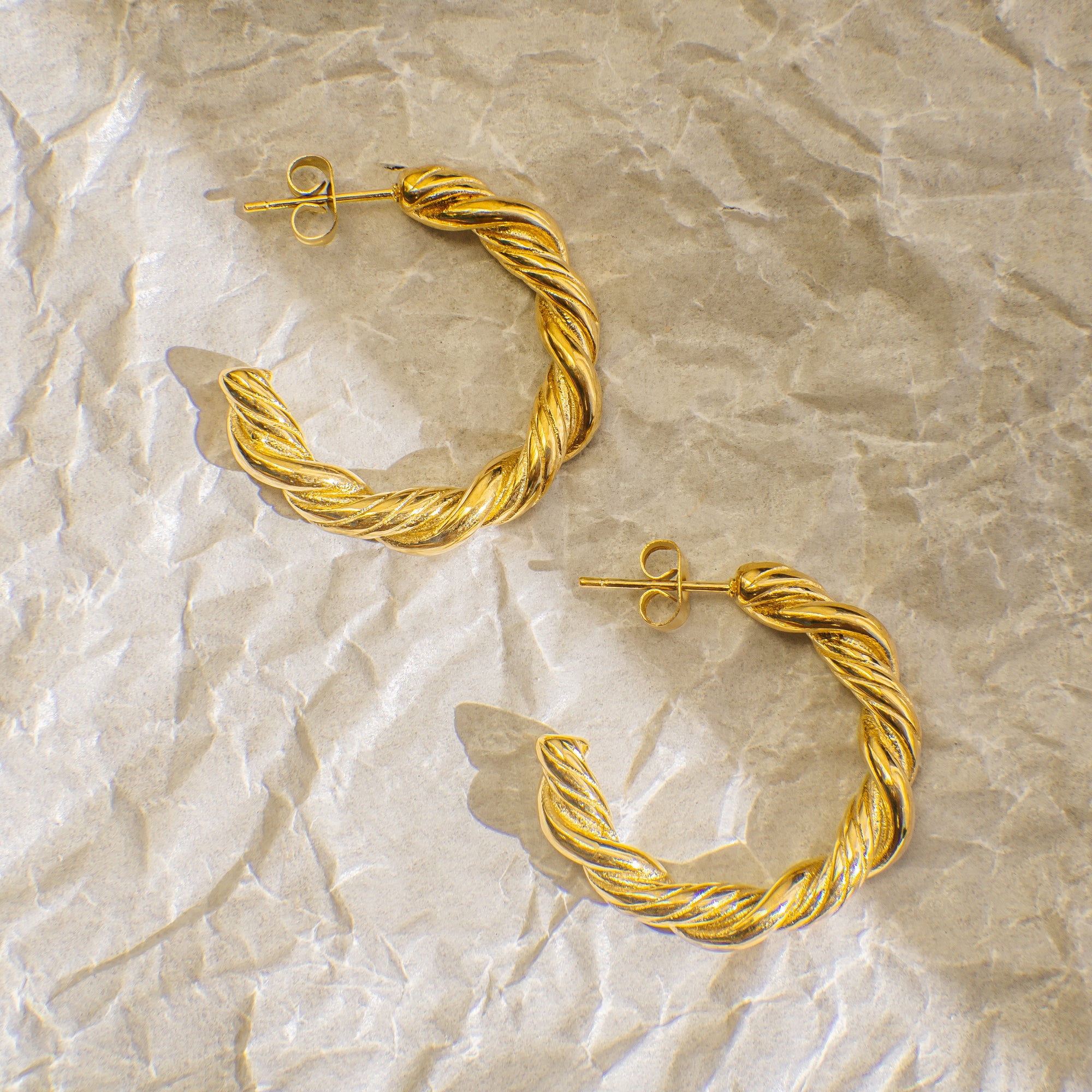 Pair of gold hoop earrings on a textured beige surface