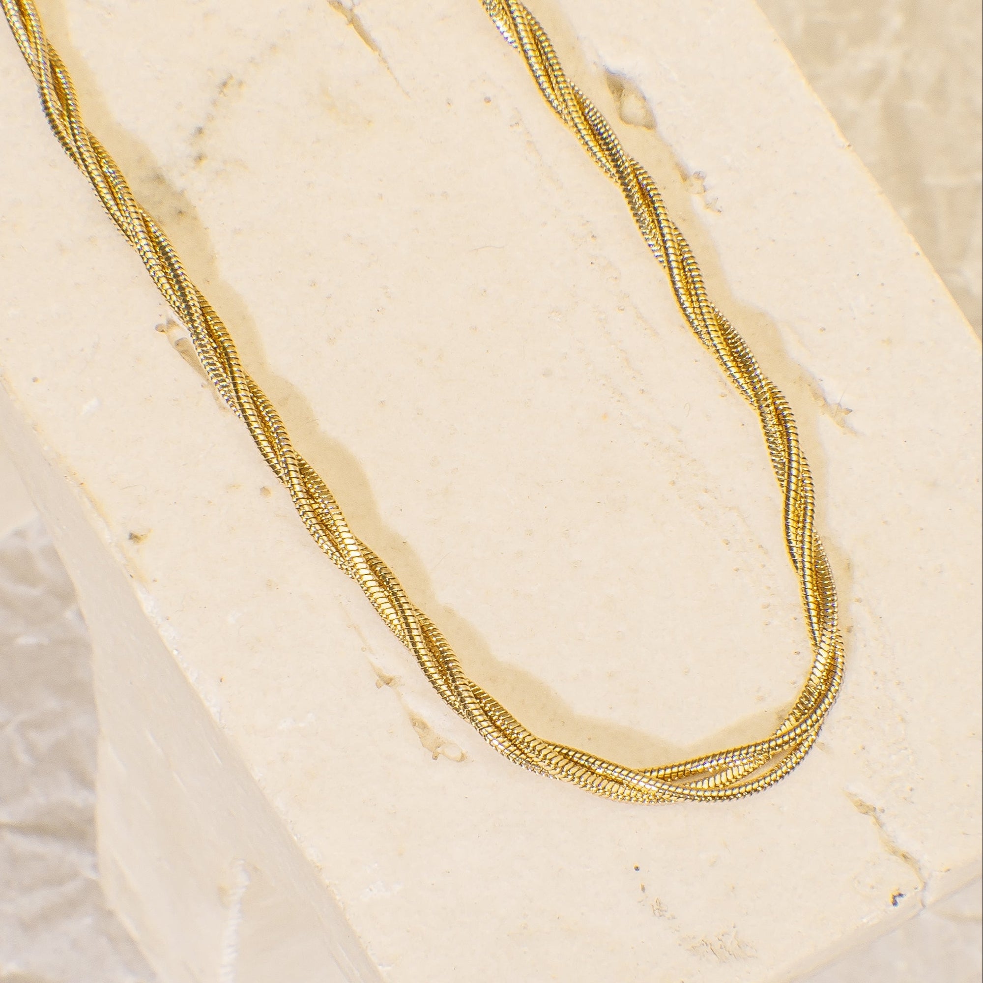 Gold necklace on a textured beige surface