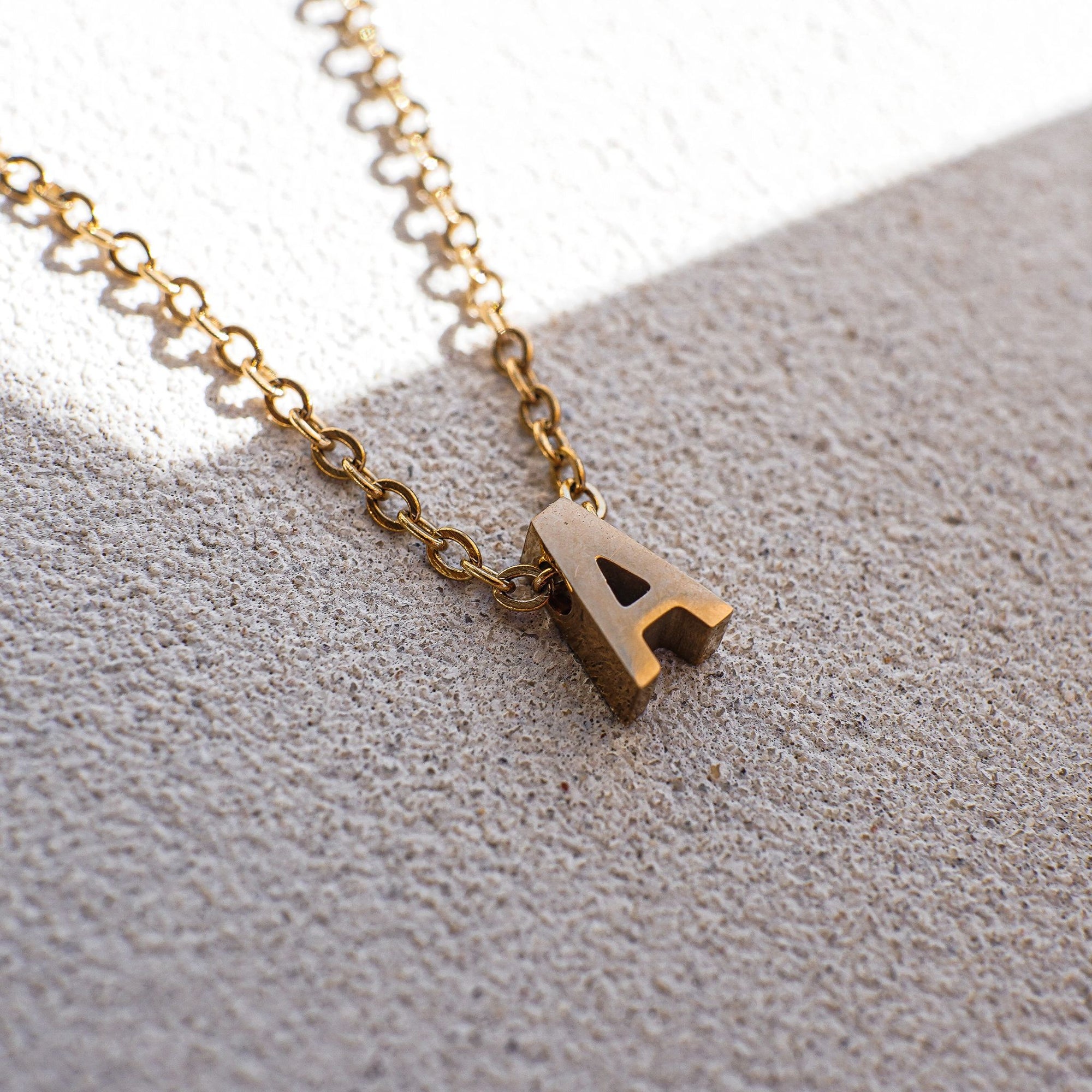 A gold necklace with letter 'A' pendant on a white textured surface