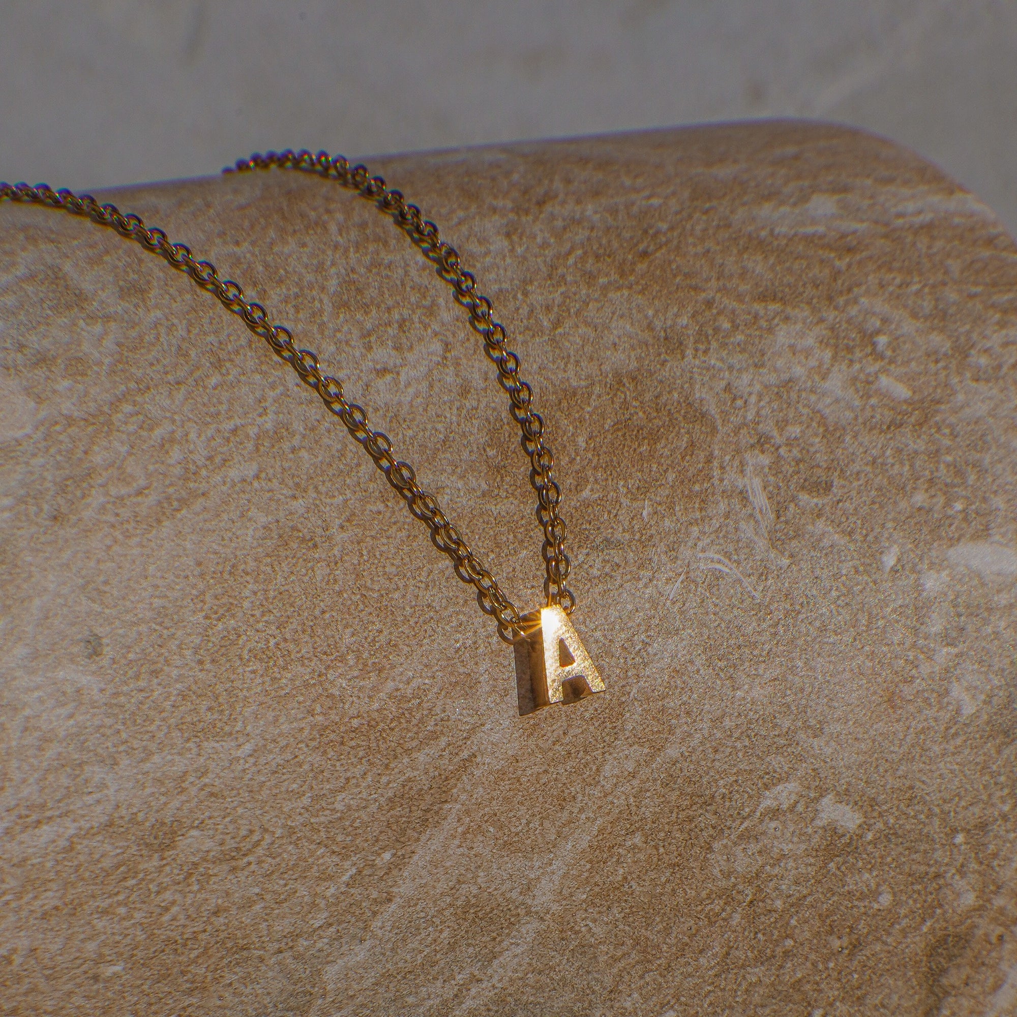 A gold necklace with letter 'A' pendant on a dark beige surface