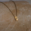 Gold necklace with a 'C' pendant on a textured beige surface