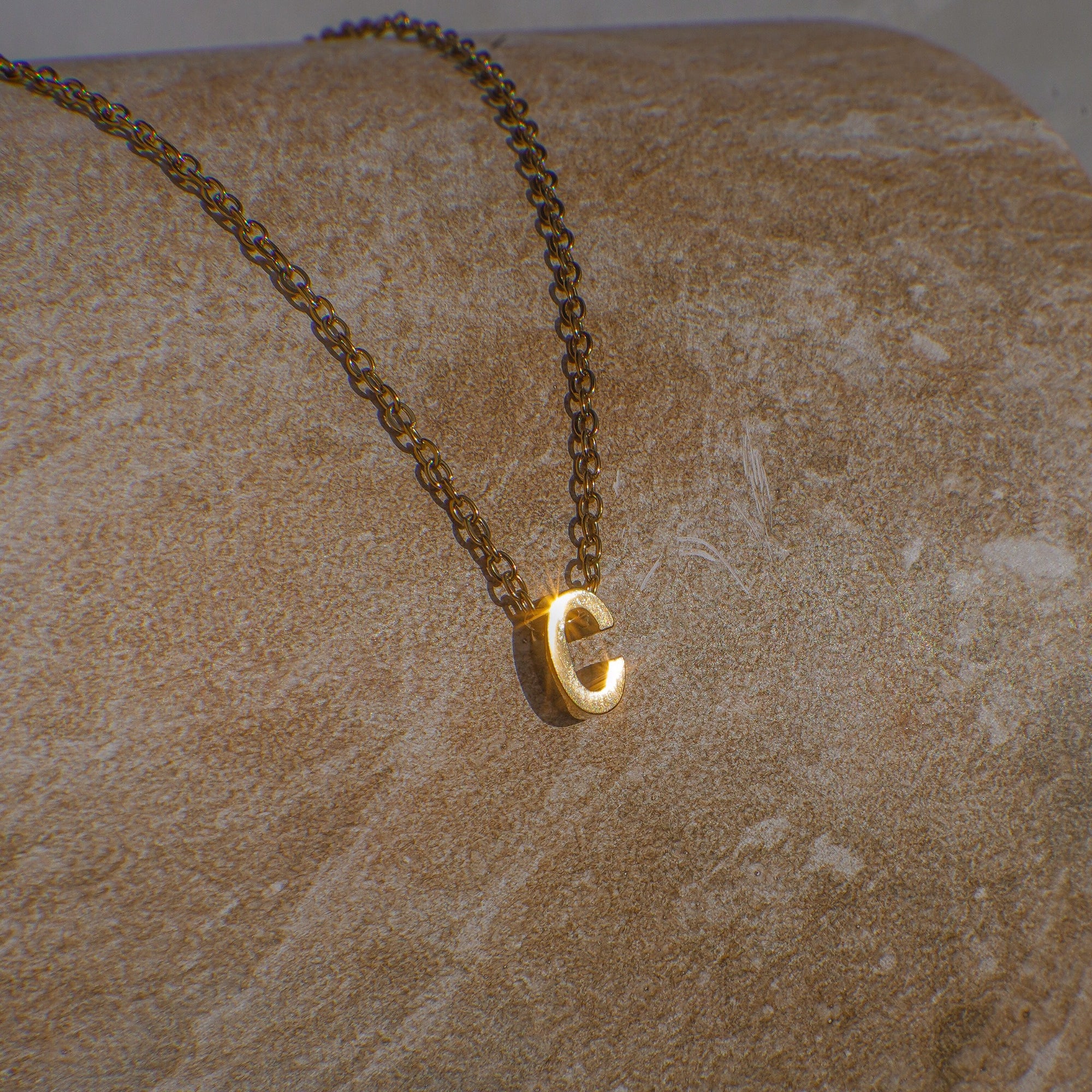 Gold necklace with a 'C' pendant on a textured beige surface