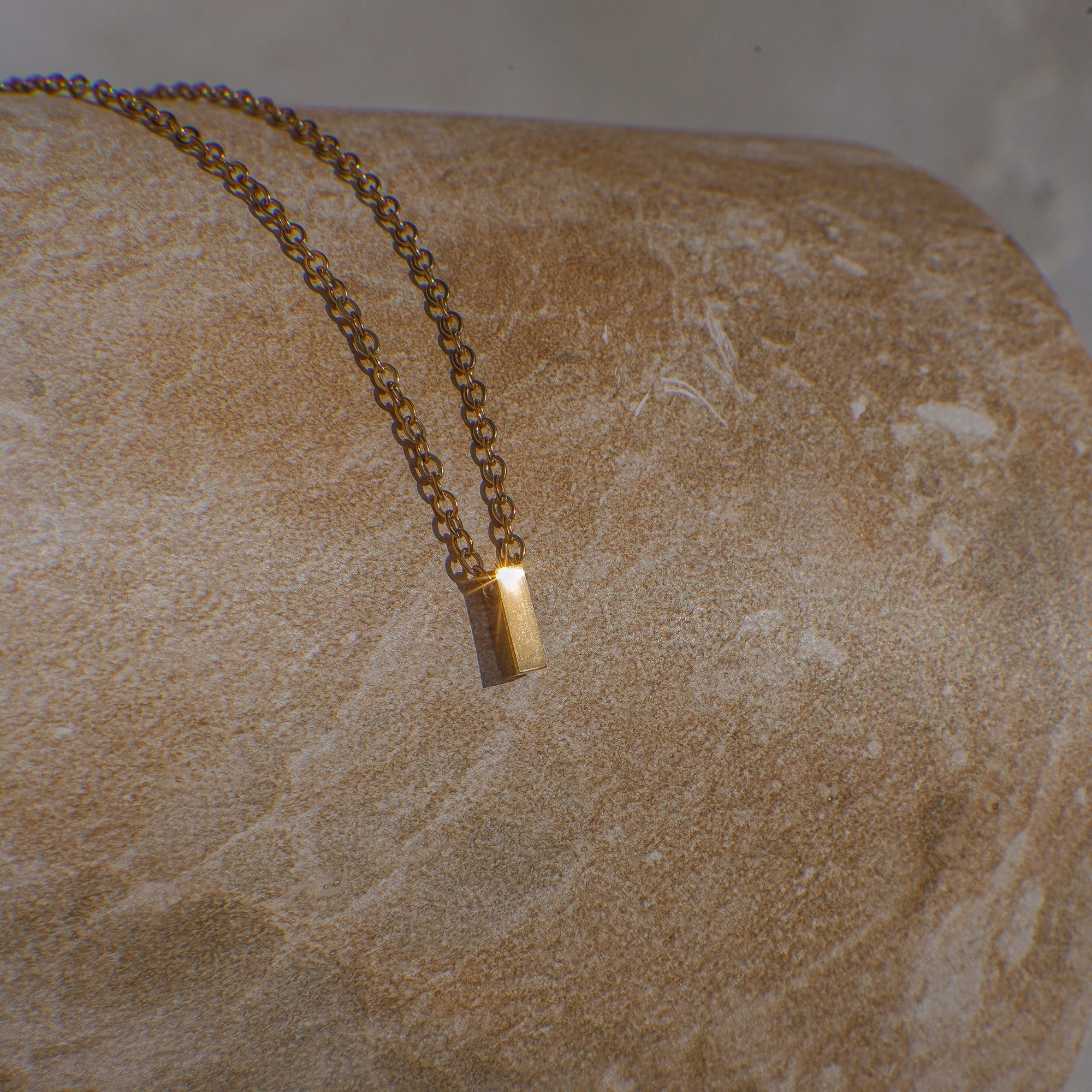 Gold necklace with a letter 'I' pendant on a stone surface