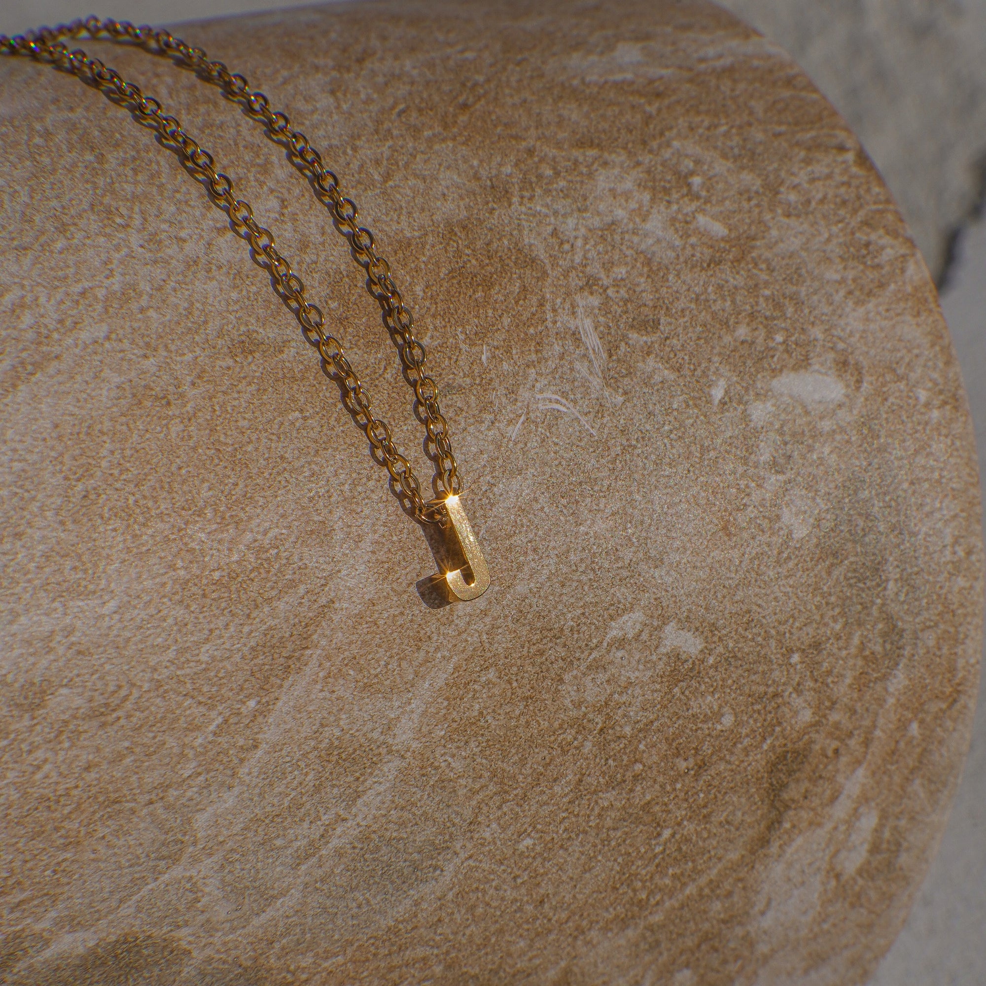 Gold necklace with letter 'J' on a textured stone surface