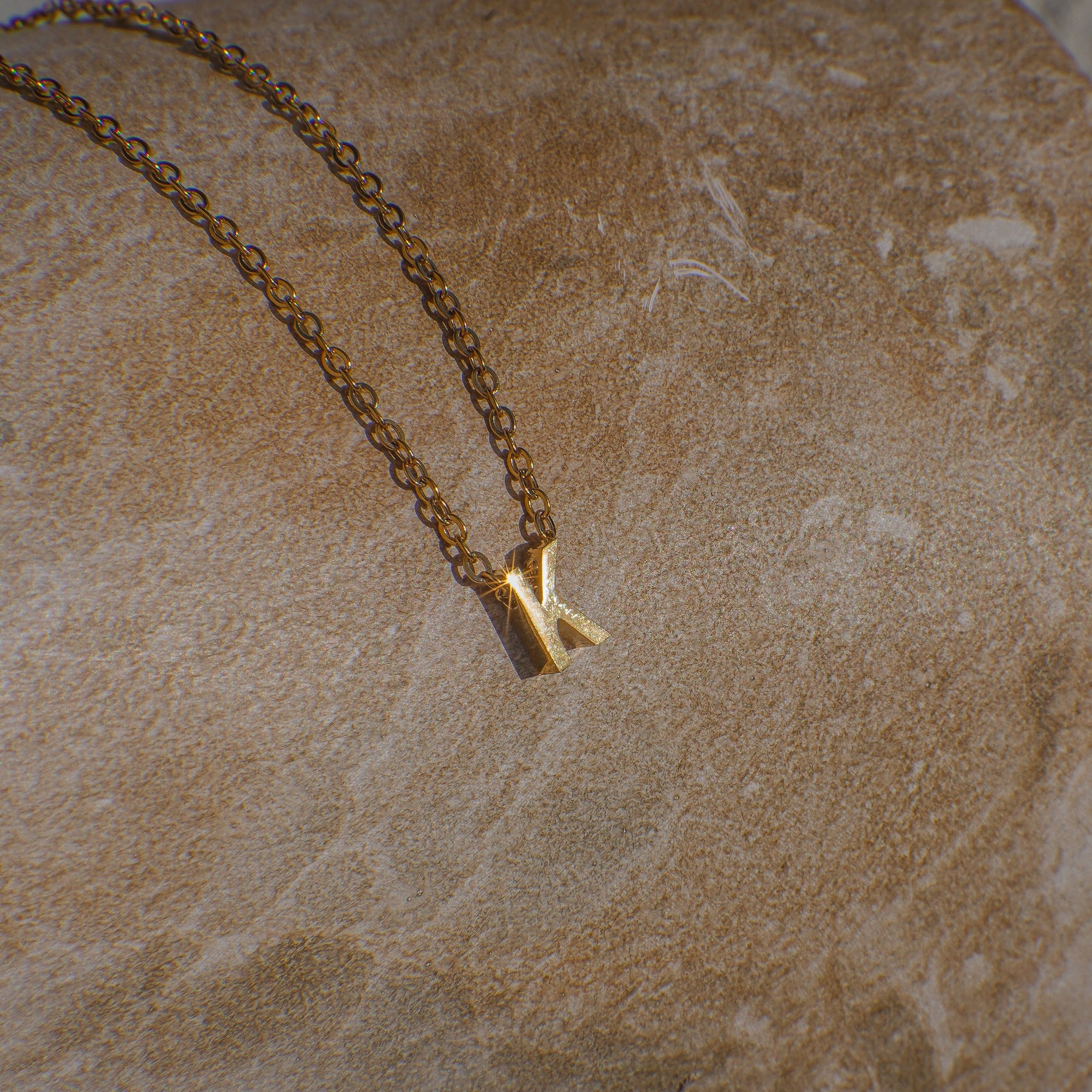 Gold necklace with a 'K' pendant on a beige marble surface