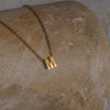 Gold necklace with a 'M' pendant on a textured stone surface